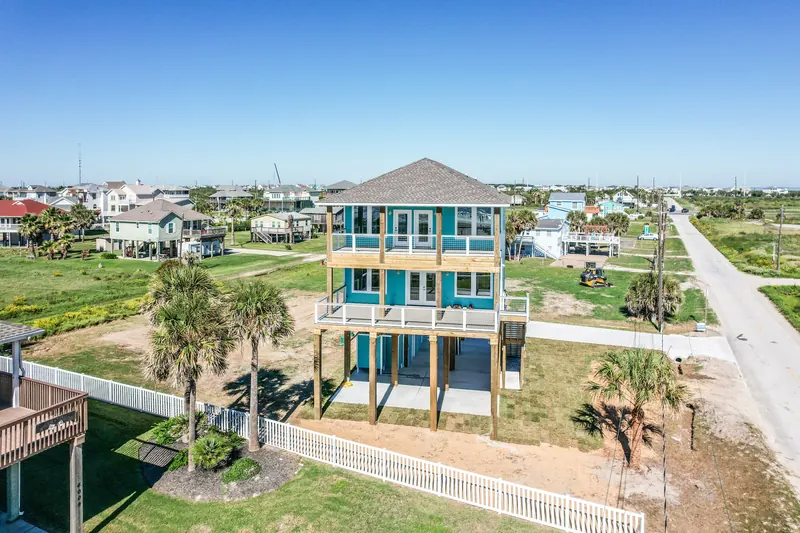 Aerial photograph of the 11 Mile custom beach home in Galveston, showing the turquoise elevated structure, palms, and surrounding West End lots