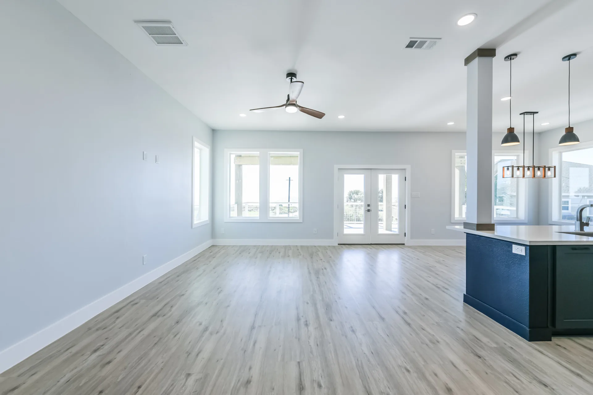 Living space at 11 Mile looking toward the kitchen, with a wall of windows and a modern ceiling fan