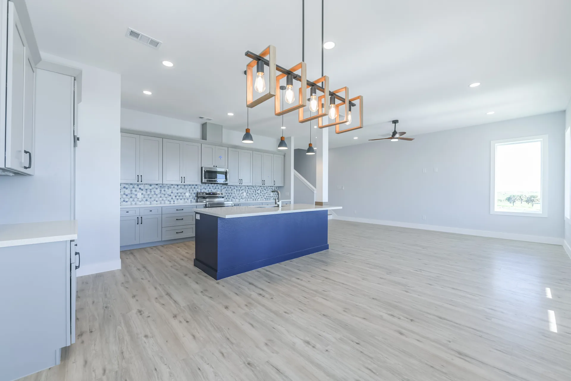 Dining area at 11 Mile with a linear chandelier above the table and the kitchen island beyond