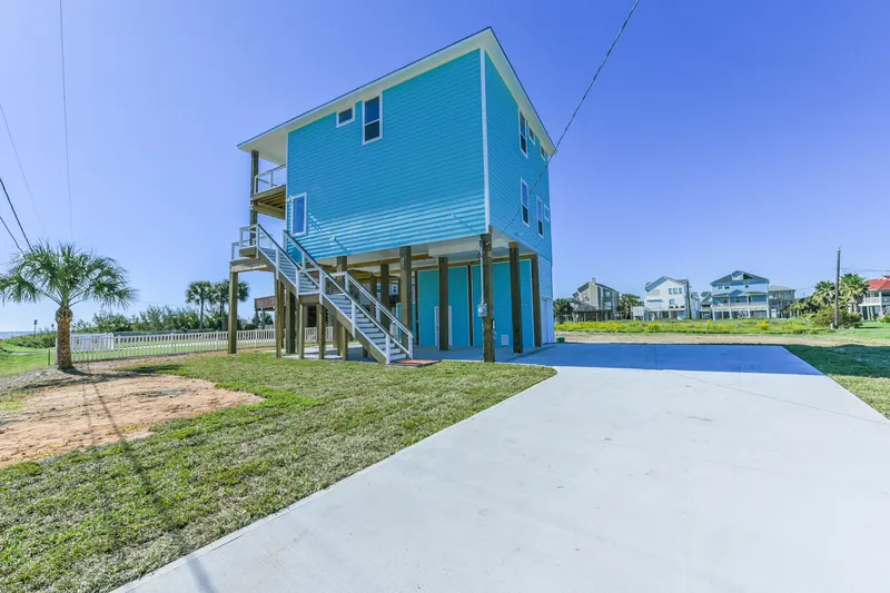 Ground-level view of the 11 Mile beach home with turquoise siding, exterior stair, and elevated pier-and-beam construction