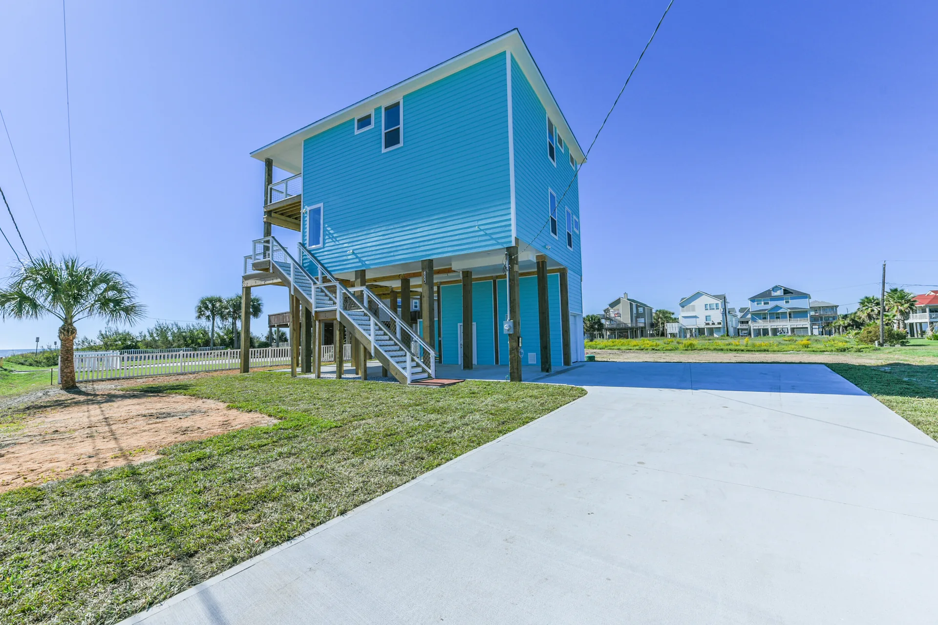 Ground-level view of the 11 Mile beach home with turquoise siding, exterior stair, and elevated pier-and-beam construction