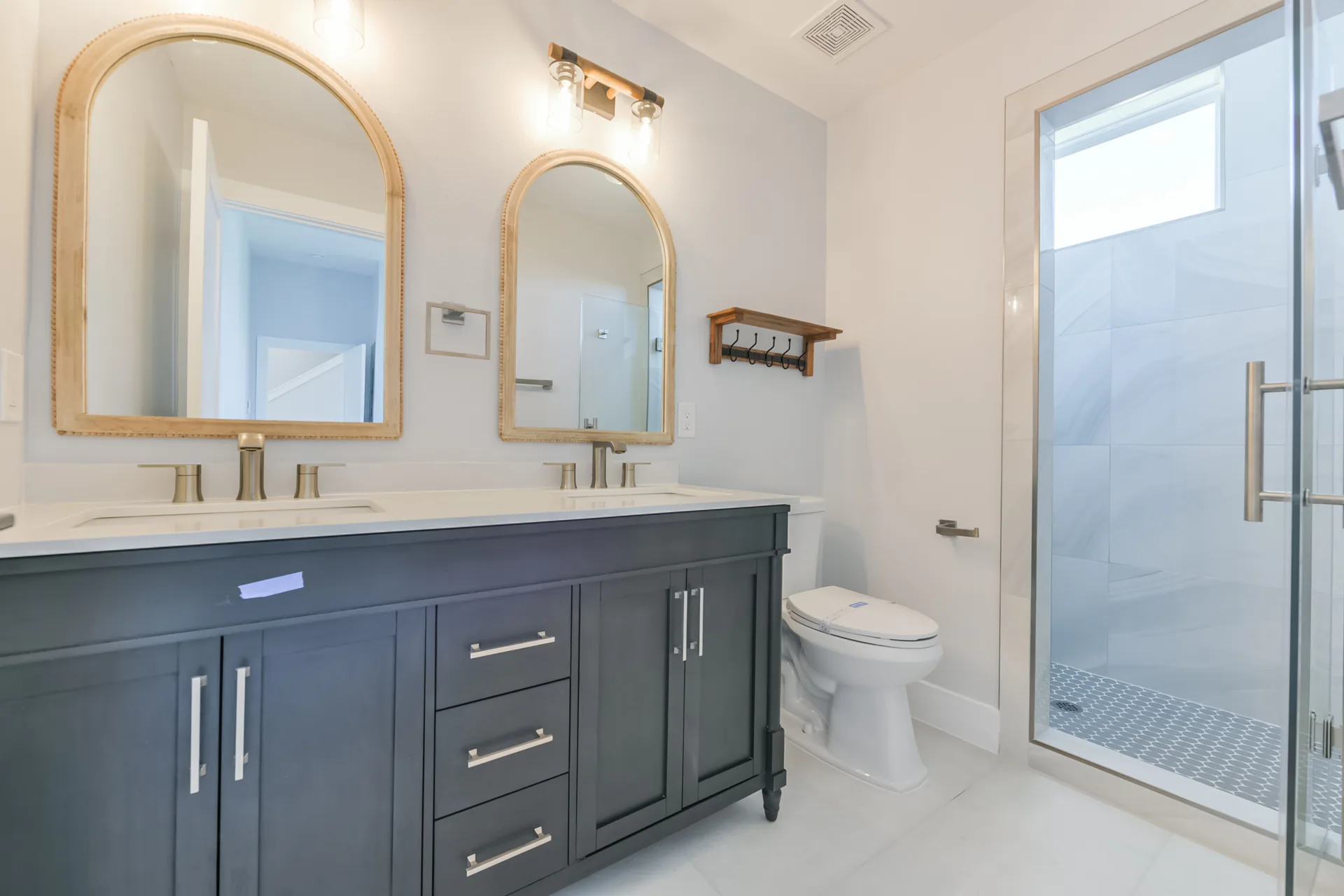 Double vanity bath at 11 Mile with dark cabinetry, arched gold-framed mirrors, and gold fixtures