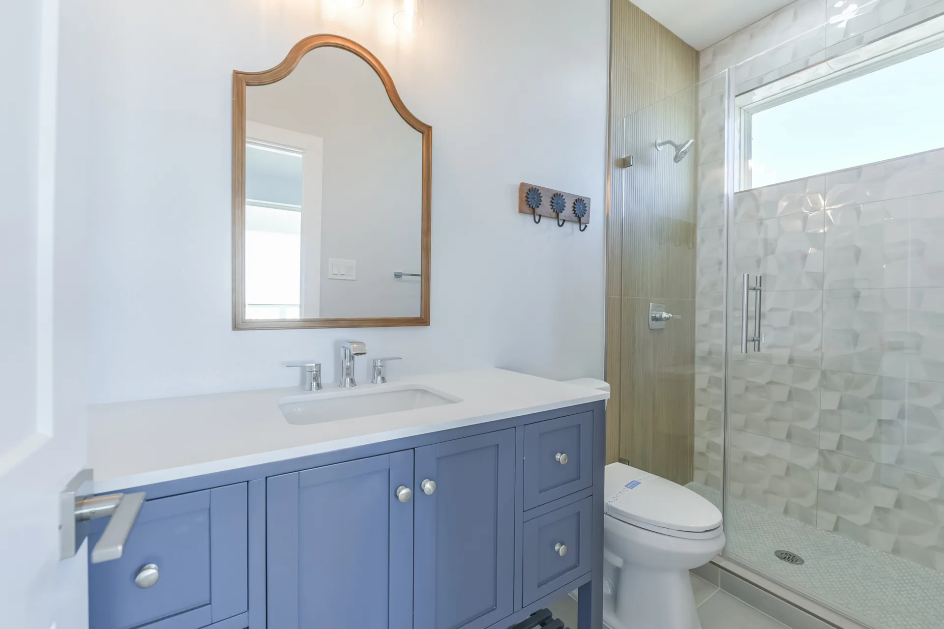 Bathroom at 11 Mile with a periwinkle blue vanity, quartz top, and glass-enclosed tile shower