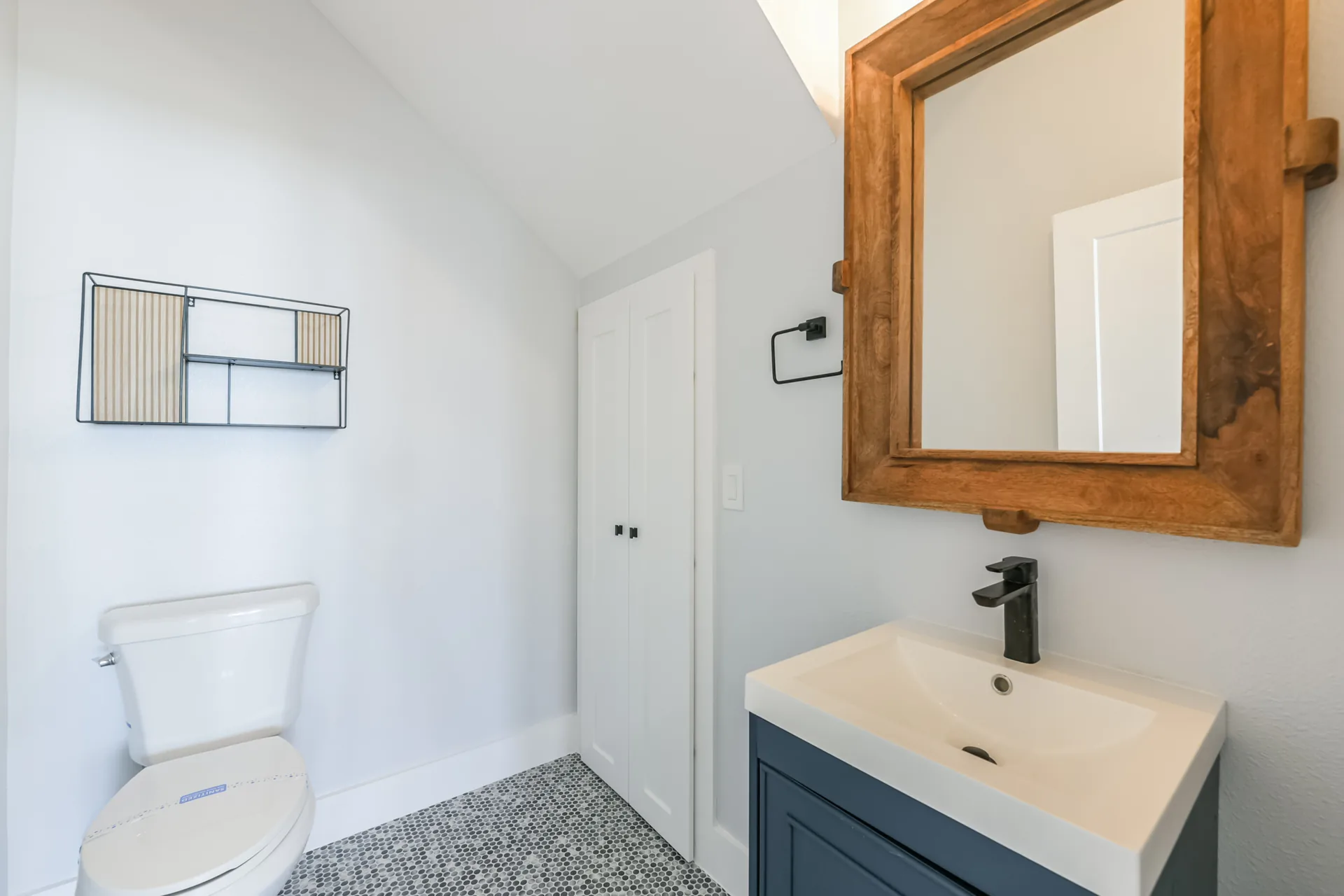 Bath at 11 Mile with a wood-framed mirror, dark vanity, matte black faucet, and pebble tile floor