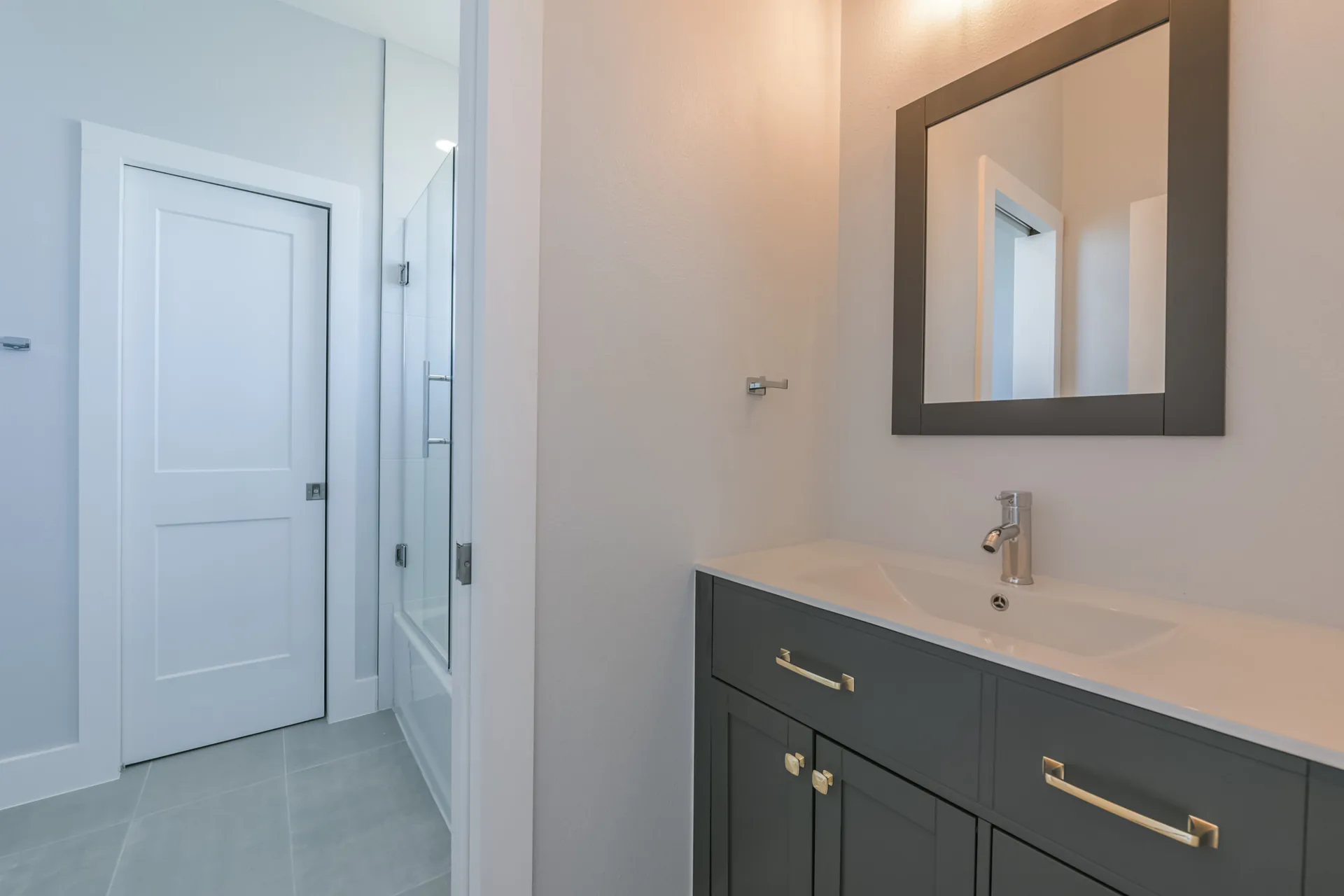 Vanity at 11 Mile with grey cabinetry, gold hardware, and a framed mirror above