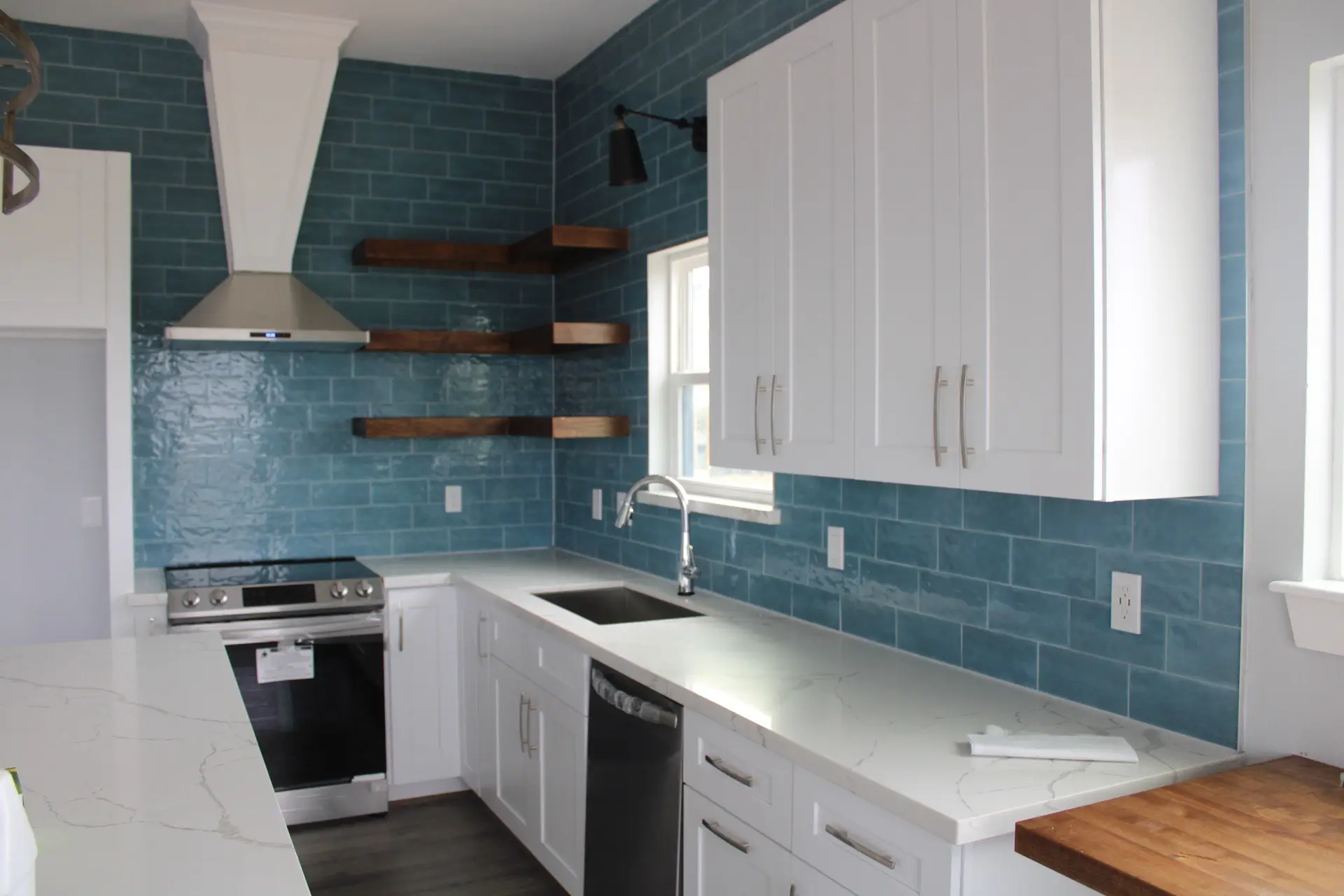 Dining area adjacent to the kitchen with contemporary wall sconces, dark plank floors, and balcony access through glass doors beyond