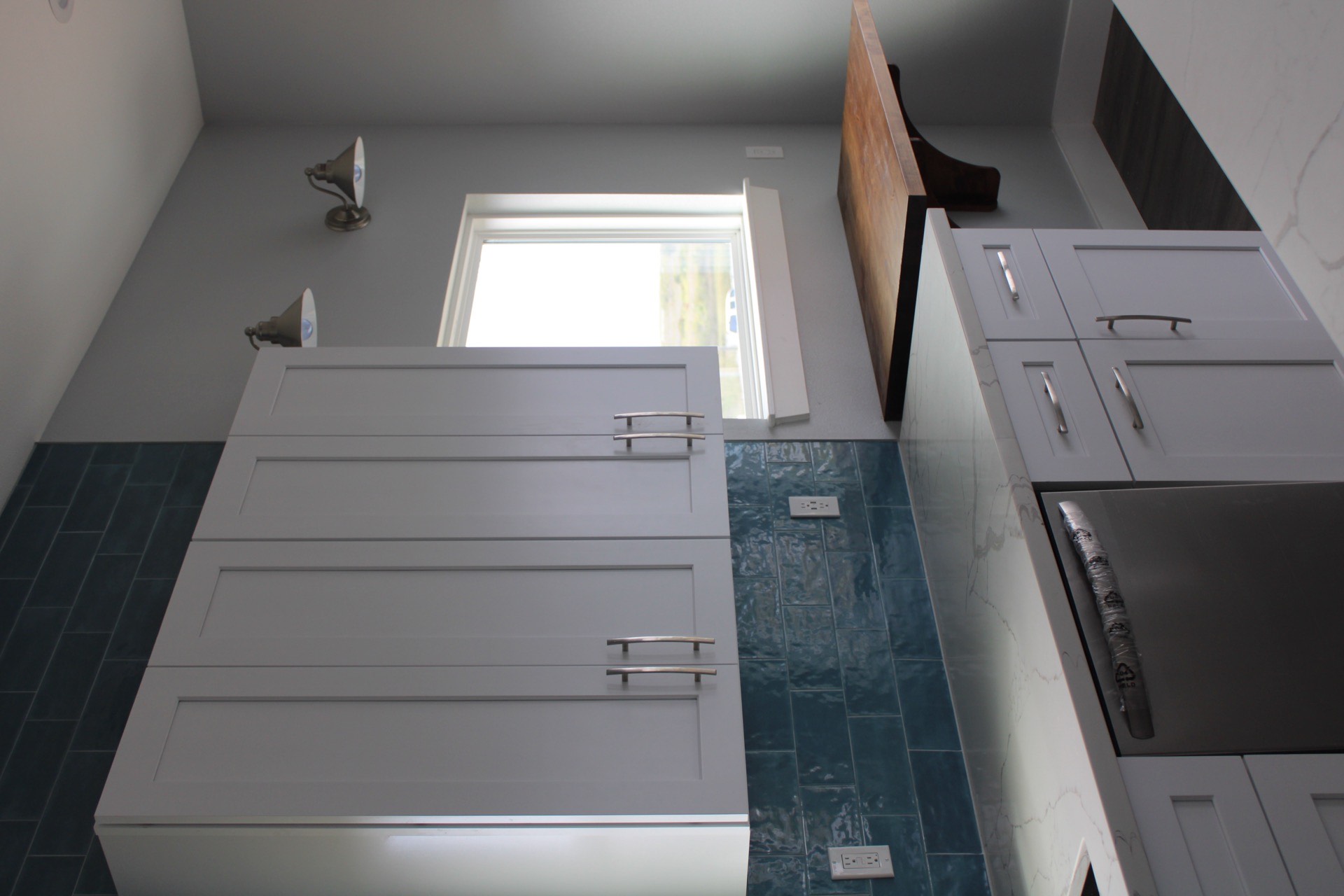 Primary bath vanity with white countertop, contemporary wall-mounted sconces, rectangular mirror, and decorative floor tile extending from the shower area