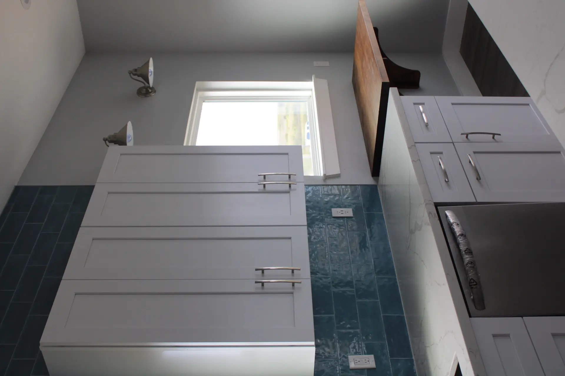 Primary bath vanity with white countertop, contemporary wall-mounted sconces, rectangular mirror, and decorative floor tile extending from the shower area