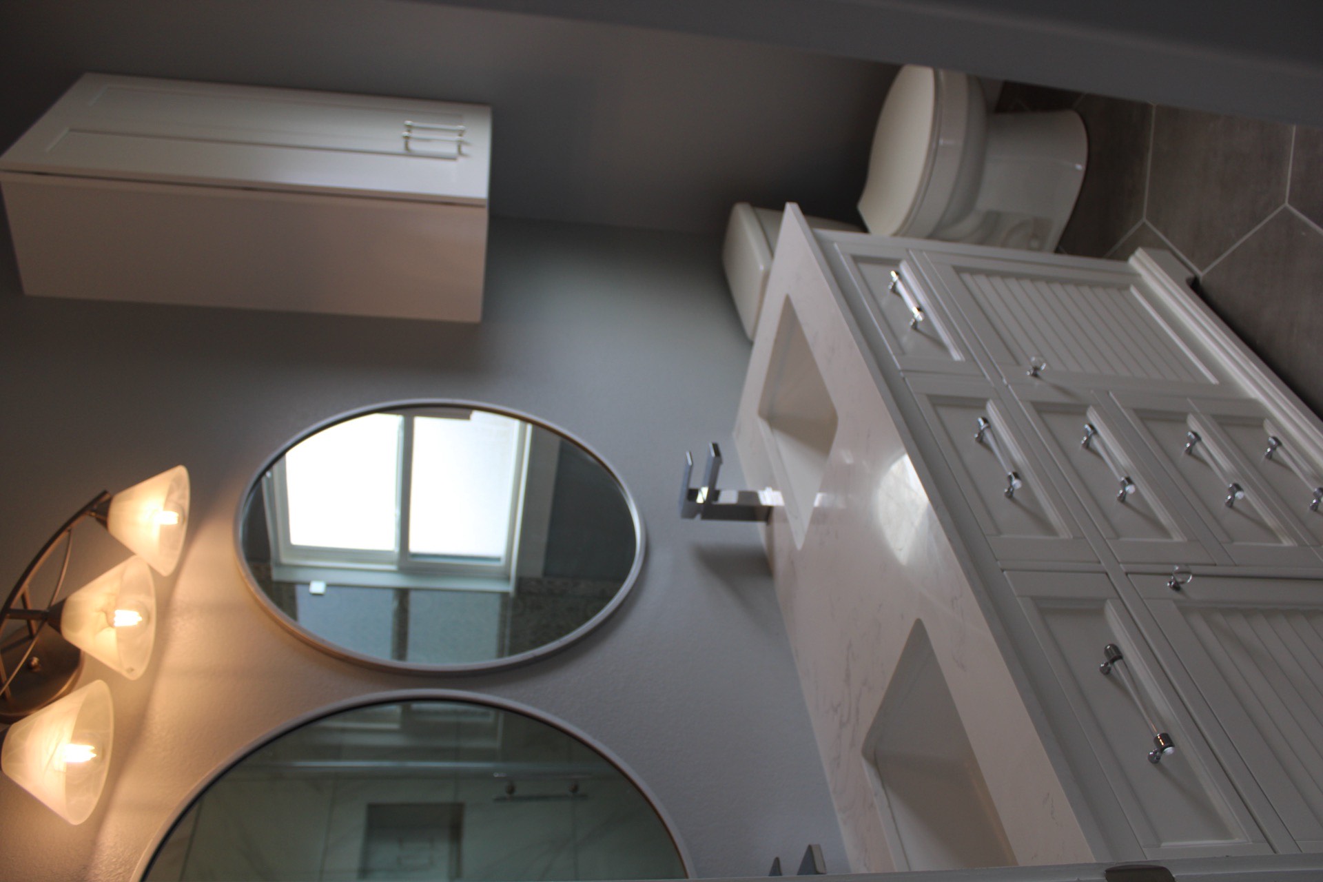 Secondary bath vanity area with clean white countertop, modern light fixture, and decorative tile floor accent complementing the marble shower tile