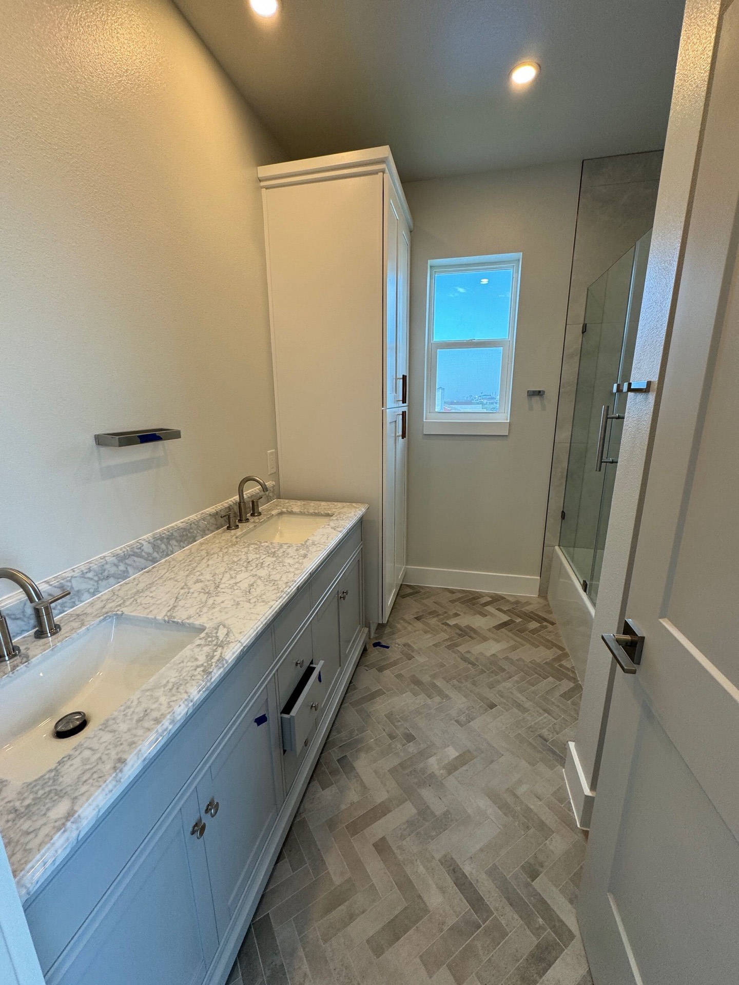 Primary bathroom with gray vanity, white marble countertop, brass faucet fixtures, and frameless glass shower enclosure