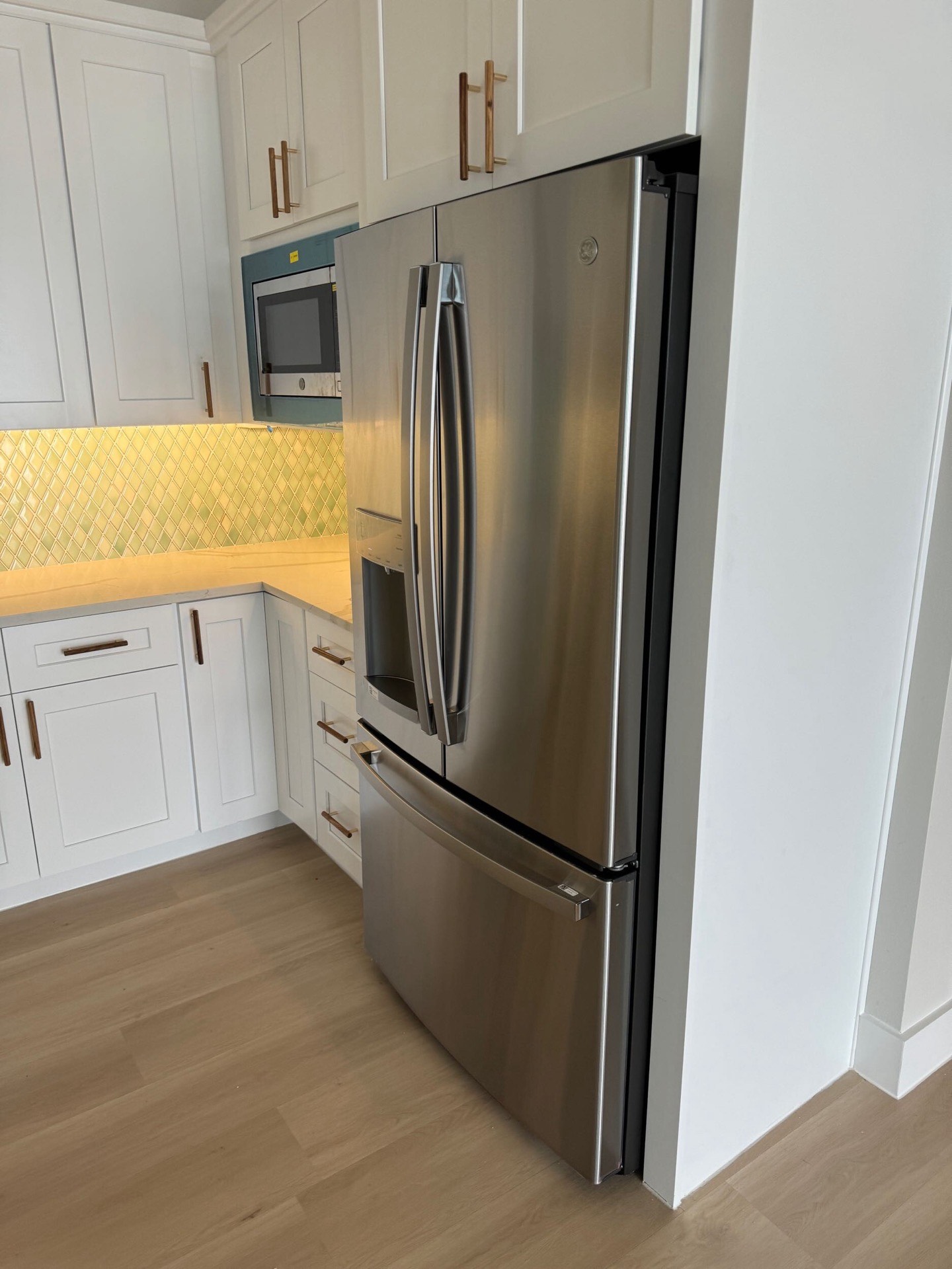 Open kitchen with white shaker cabinetry, gold brass cabinet hardware, quartz countertops, and light oak hardwood flooring throughout