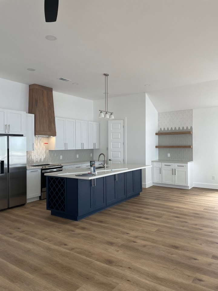 Wide-angle view of the open-concept kitchen flowing into the living area with light oak hardwood floors and abundant natural light