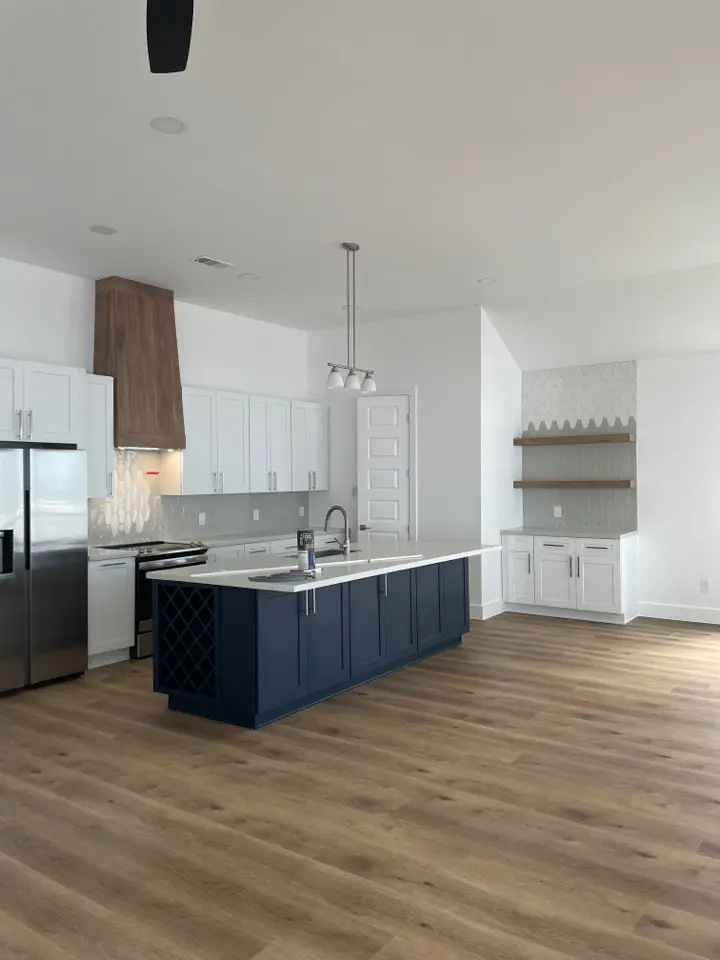 Wide-angle view of the open-concept kitchen flowing into the living area with light oak hardwood floors and abundant natural light