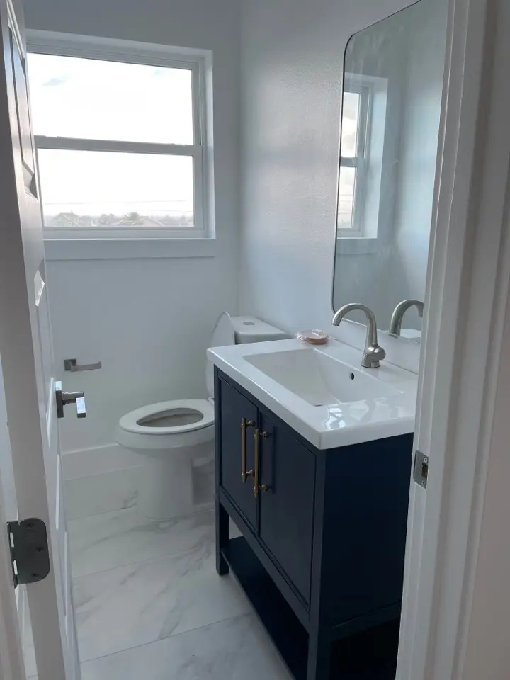 Master bathroom vanity area with illuminated mirror, navy cabinetry, gold hardware pulls, and white quartz countertop surface