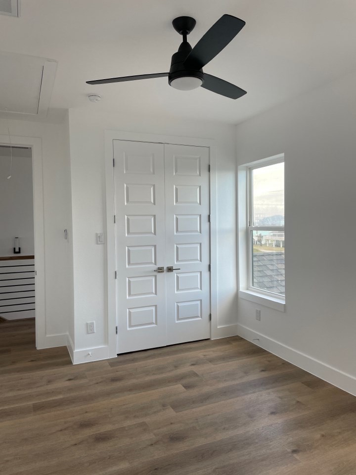 Secondary bedroom with light oak flooring, large window with coastal views, and neutral wall tones in the Gulf Drive custom home