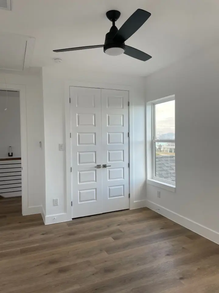 Secondary bedroom with light oak flooring, large window with coastal views, and neutral wall tones in the Gulf Drive custom home