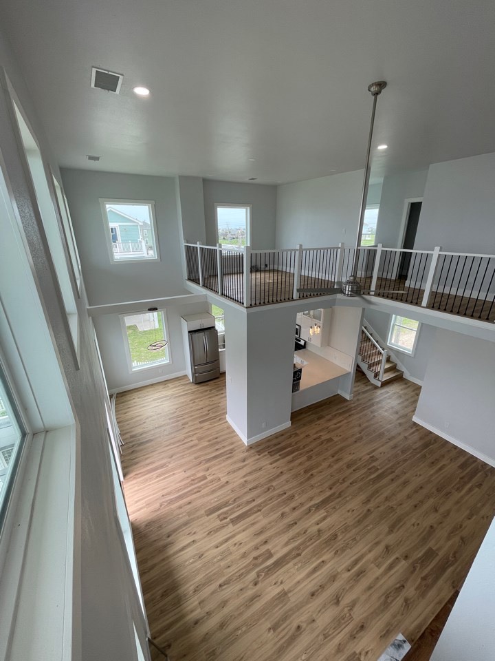 View from the upper mezzanine looking down into the open-concept living space with oversized windows flooding the interior with sunlight