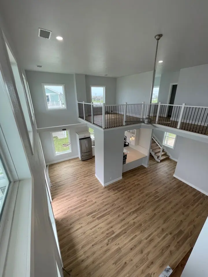 View from the upper mezzanine looking down into the open-concept living space with oversized windows flooding the interior with sunlight