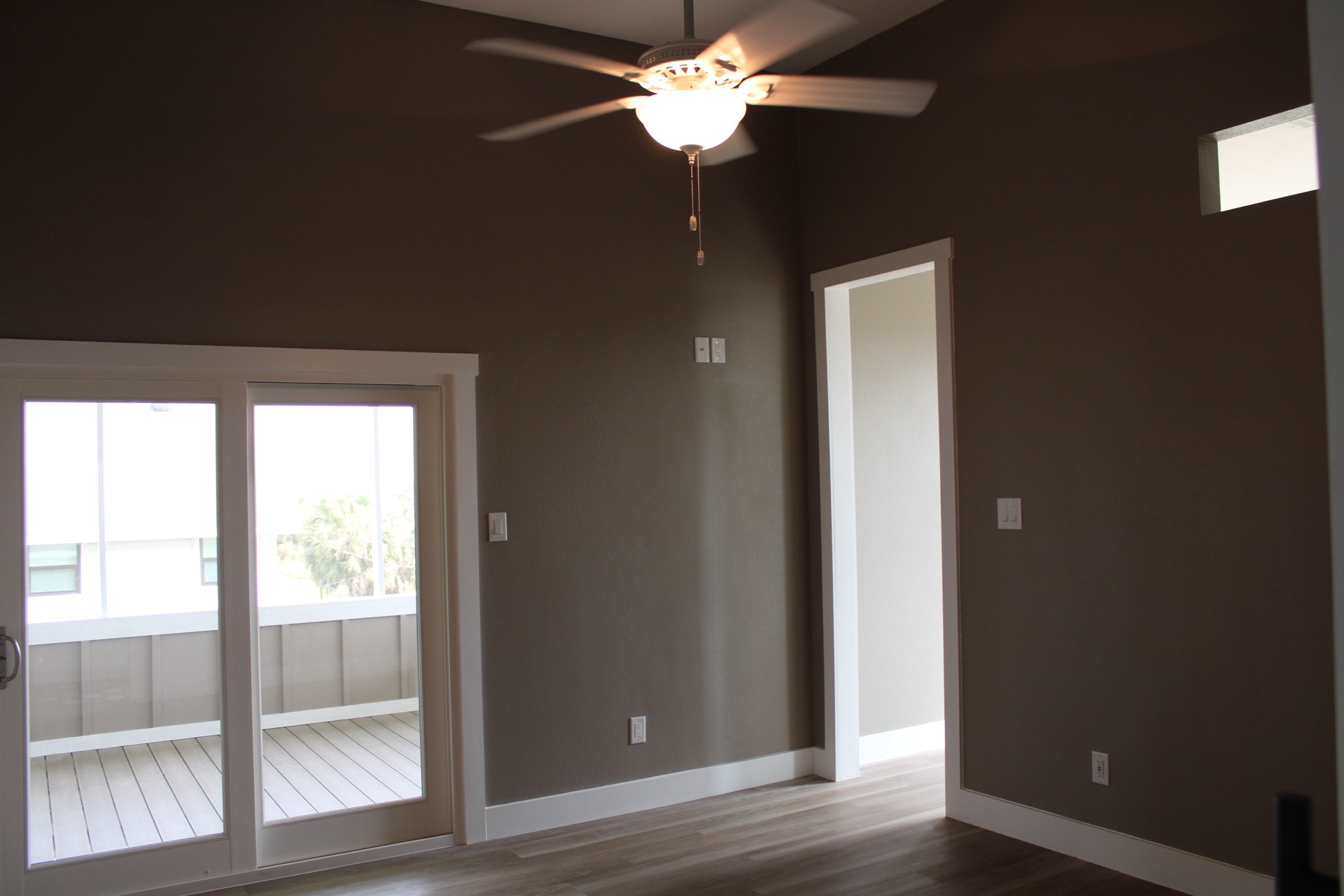 Master bedroom with French sliding doors opening to the covered deck, dark warm brown accent wall, and LVP wood-look flooring at 27 Laguna