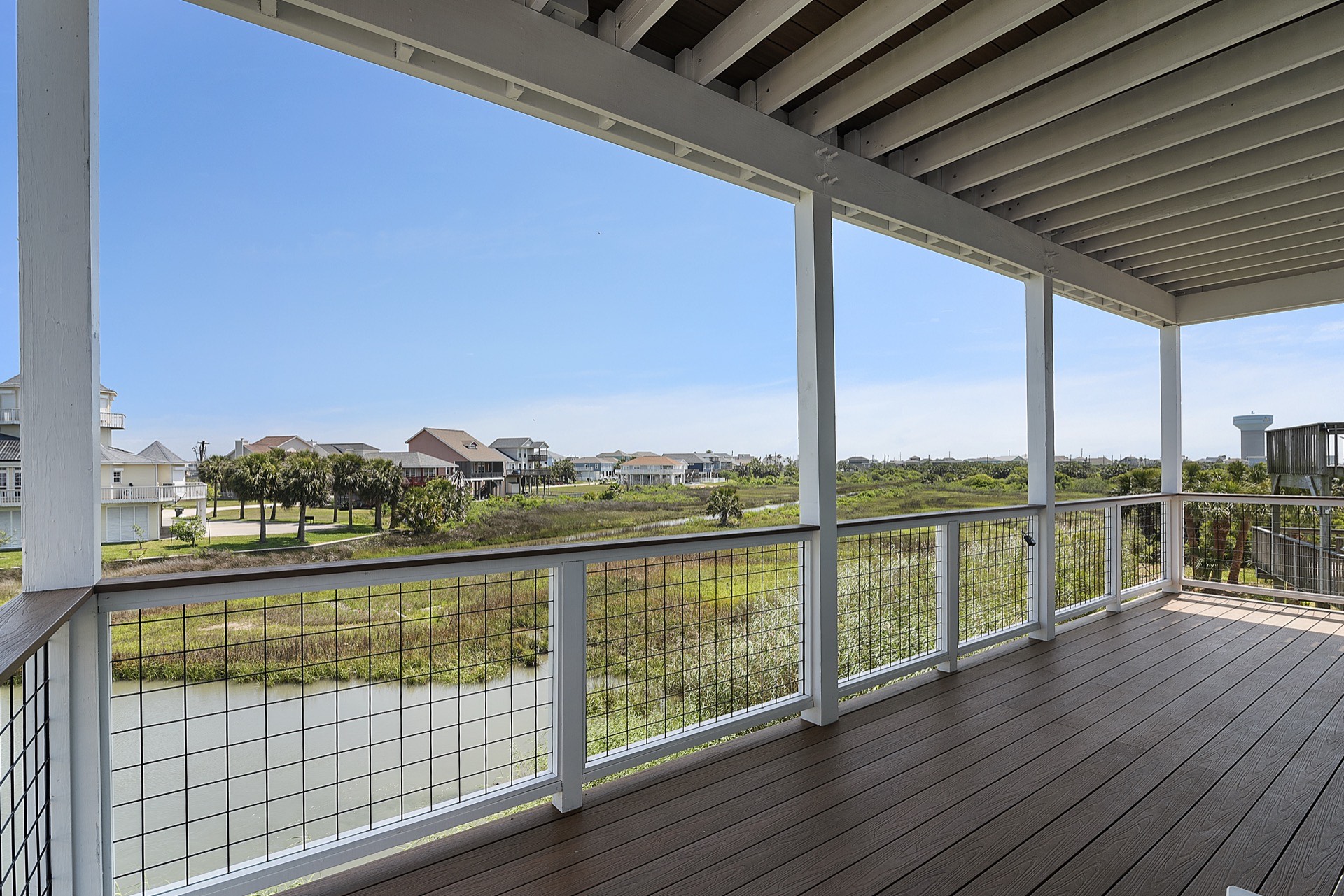Upper-level balcony with cable railing overlooking the canal, marsh grasses, and distant Galveston Bay from 3742 Laguna