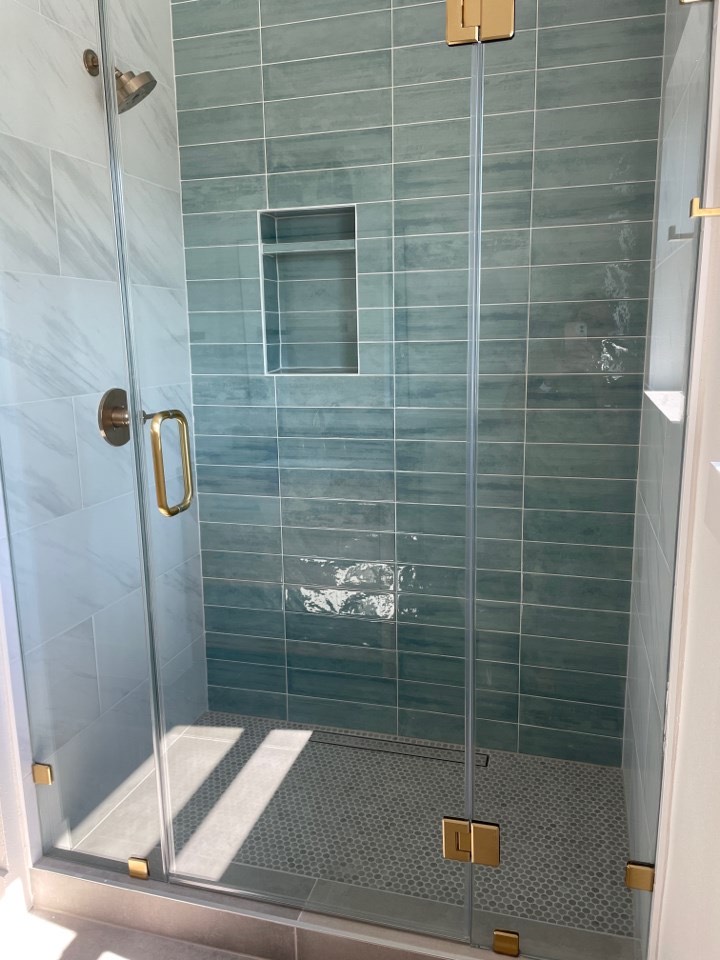 Third bathroom with clean white tile shower, modern fixtures, and waterproof LVP flooring continuing the warm wood tone from the main living areas