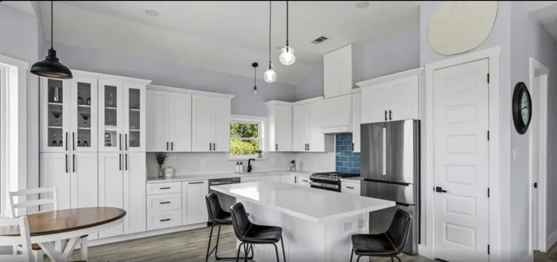 White kitchen at 5th St Seabrook with shaker cabinetry, quartz counters, pendant lighting, and a dining table
