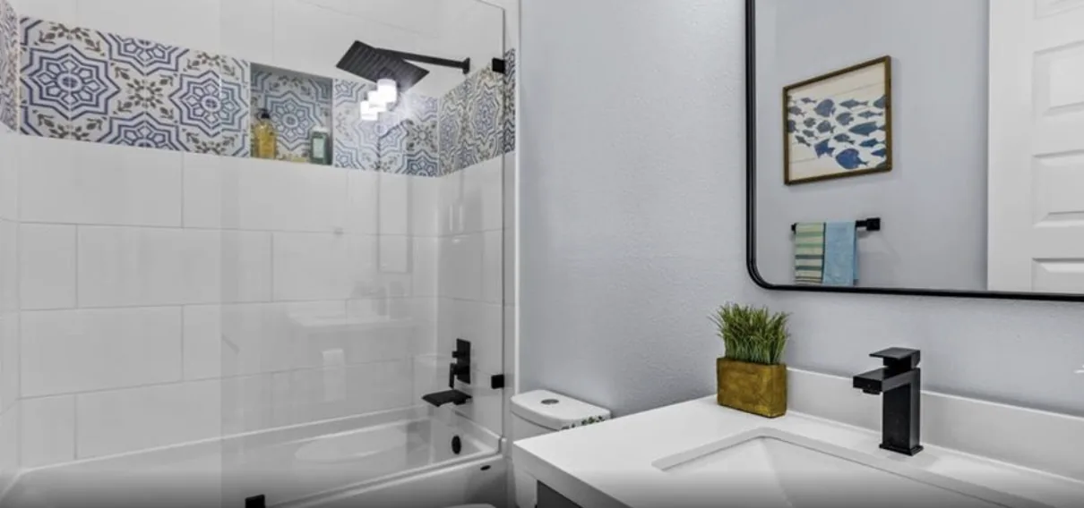 Tub bath at 5th St Seabrook with patterned accent tile, matte black fixtures, and a white vanity