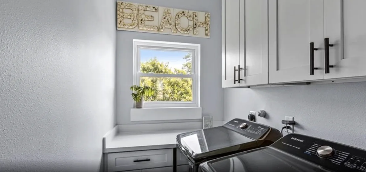 Laundry room at 5th St Seabrook with white upper cabinetry, a window, and side-by-side washer and dryer