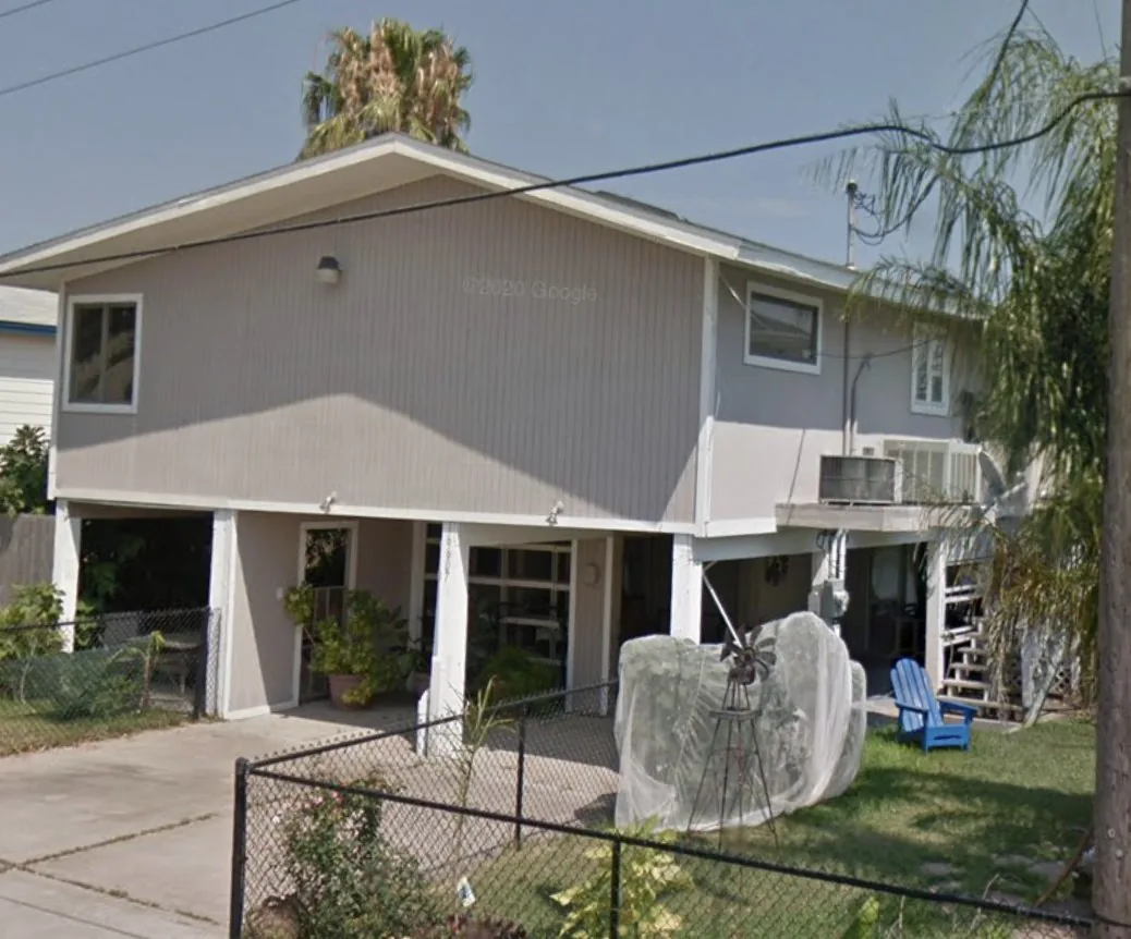 Before: original exterior of the Flounder house in Bayou Vista with grey siding, lattice skirting, and a fenced yard