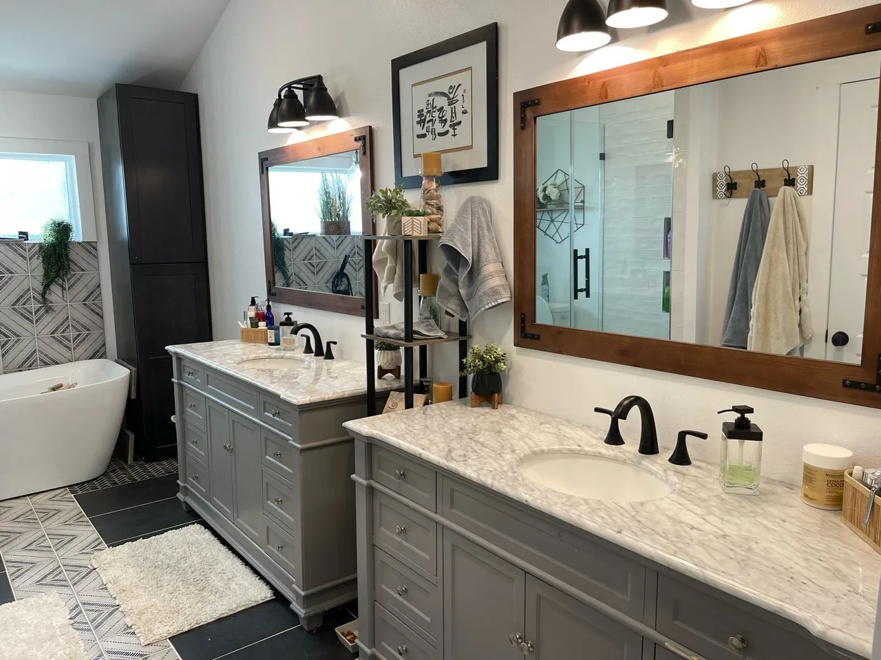 After: renovated primary bath with a double vanity, wood-framed mirrors, black fixtures, and patterned tile flooring