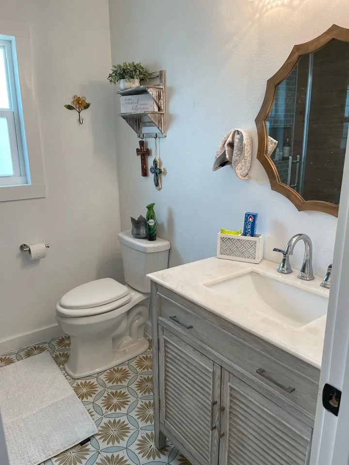 After: renovated hall bath at the Flounder house with a white vanity, wood mirror, and patterned encaustic floor tile
