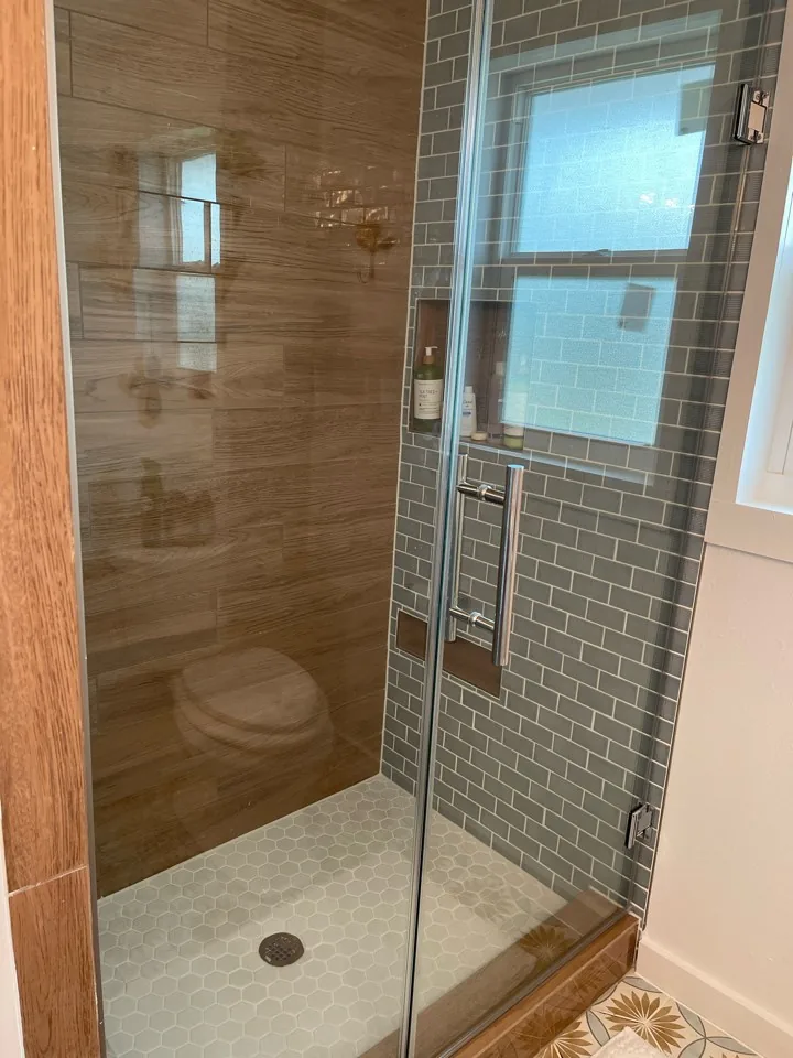 After: renovated walk-in shower with subway wall tile, a cedar-trimmed opening, and frameless glass door