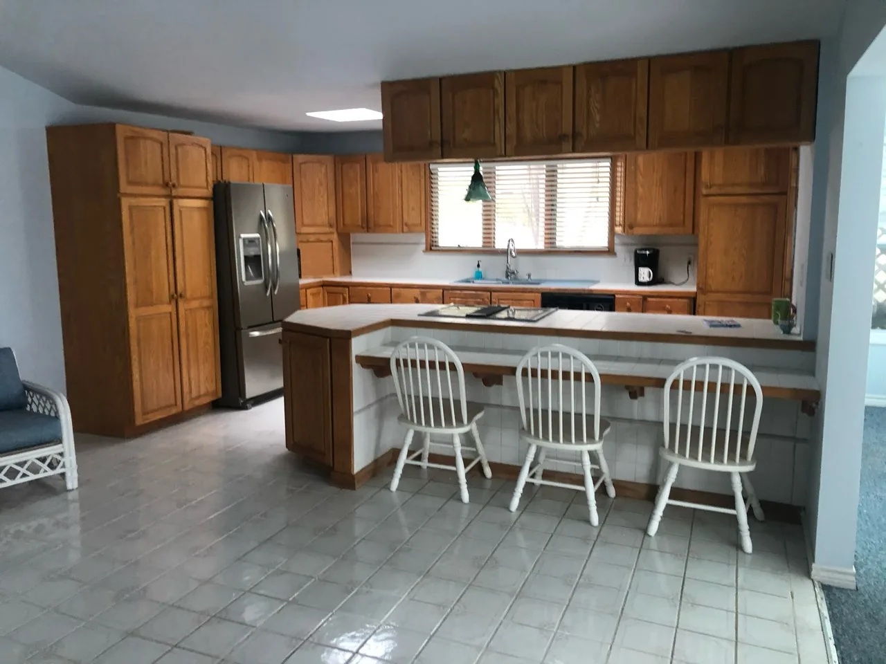 Before: original kitchen with oak cabinetry, tile counters, a peninsula with bar stools, and tile flooring