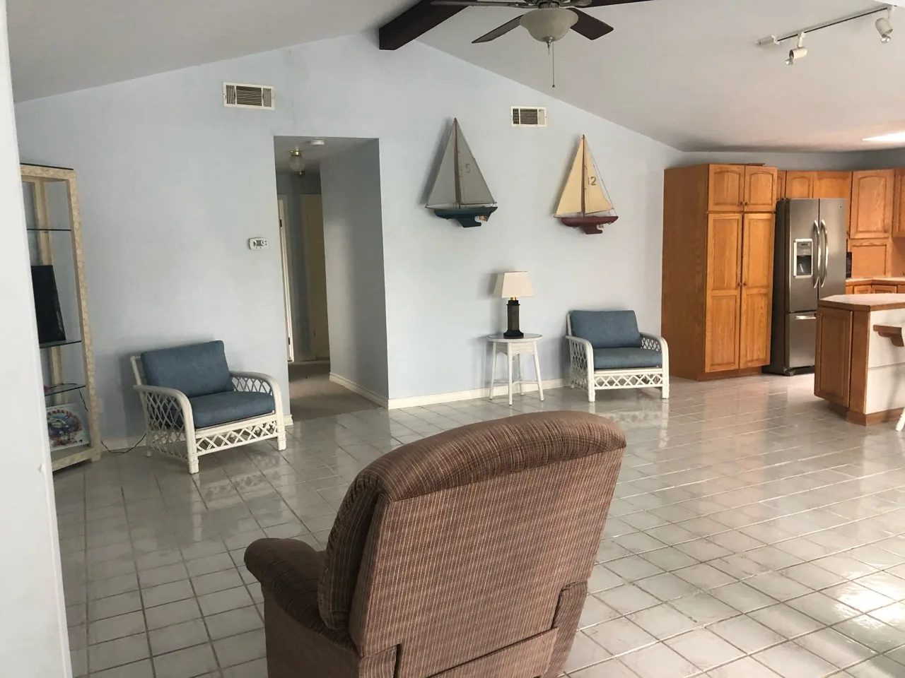 Before: original living area with tile flooring, dated furnishings, and a partial wall closing off the kitchen