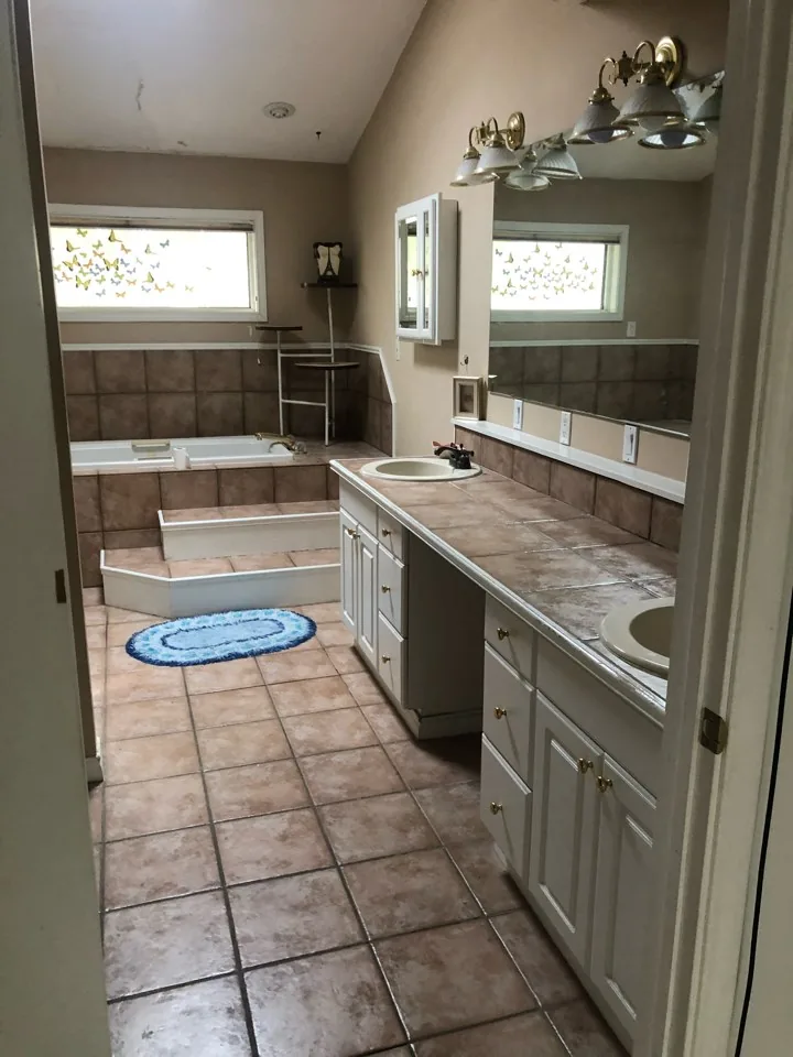 Before: original primary bath with a corner garden tub, tile deck, laminate counters, and oak cabinetry