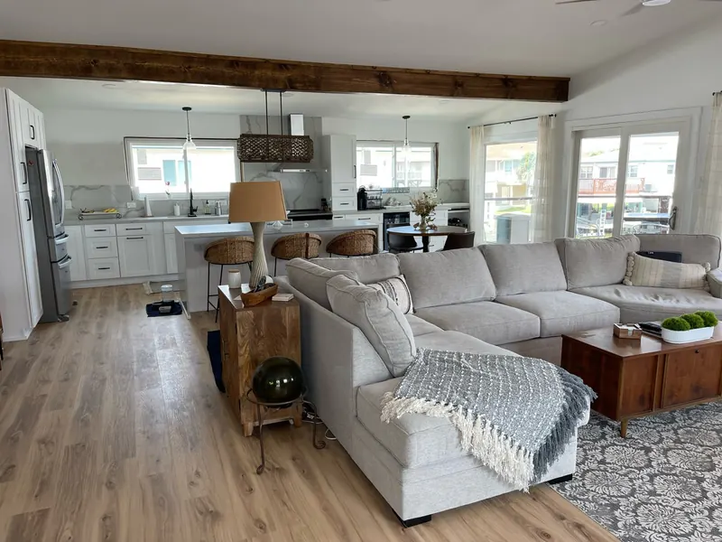 After: open living and kitchen at the Flounder renovation, unified under an exposed beam ceiling with wood-look flooring