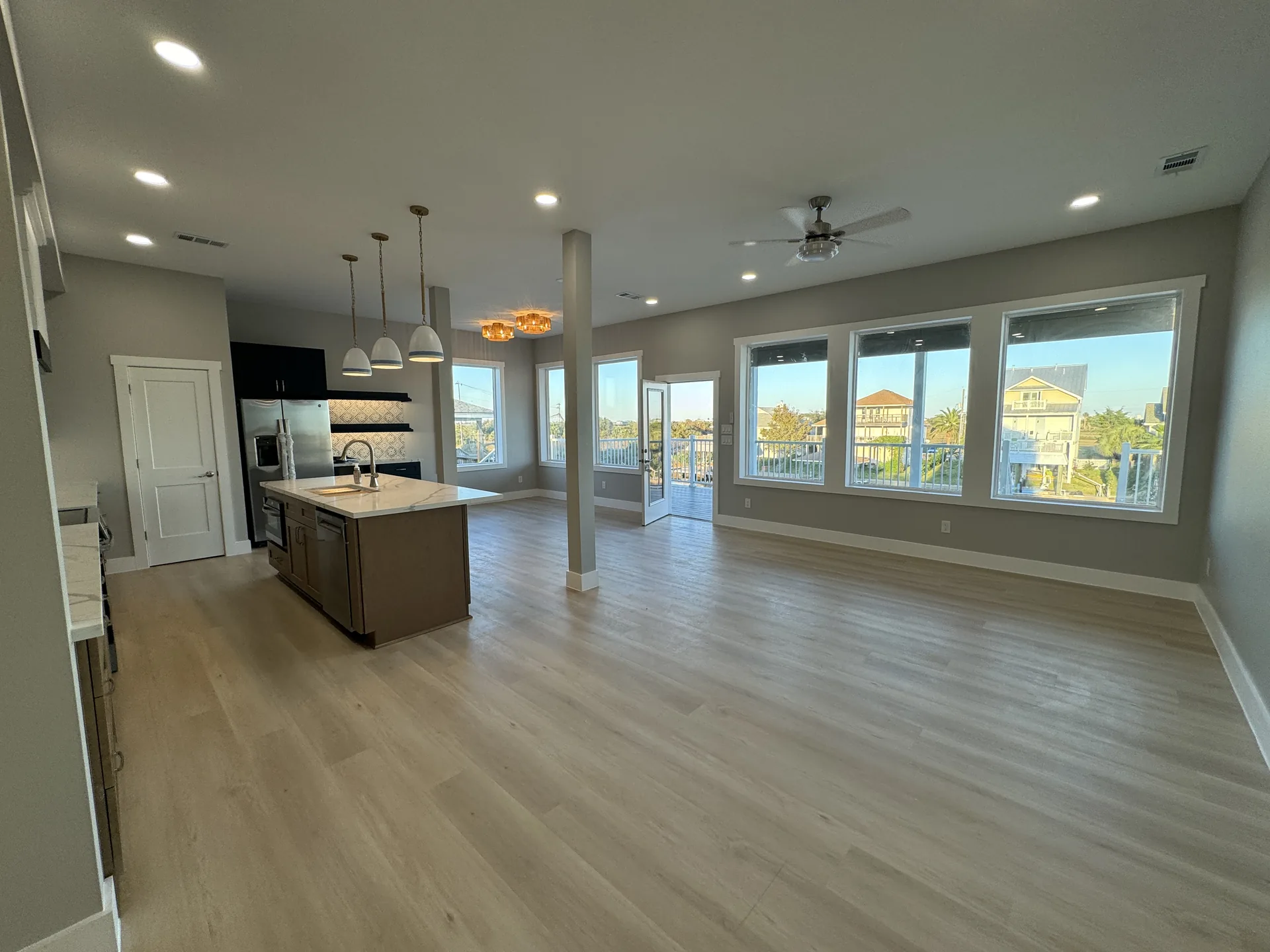 Open great room at Galleon looking toward the kitchen, with light wood-look flooring and a wall of windows to the water