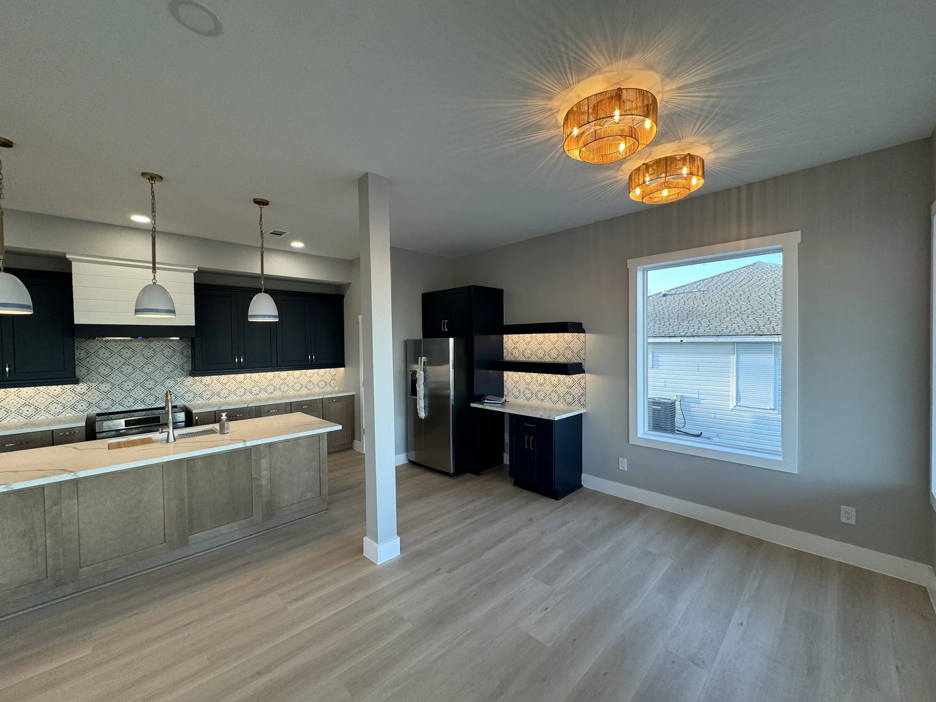 Galleon kitchen with dark navy cabinetry, stainless appliances, tile backsplash, and a woven drum pendant fixture