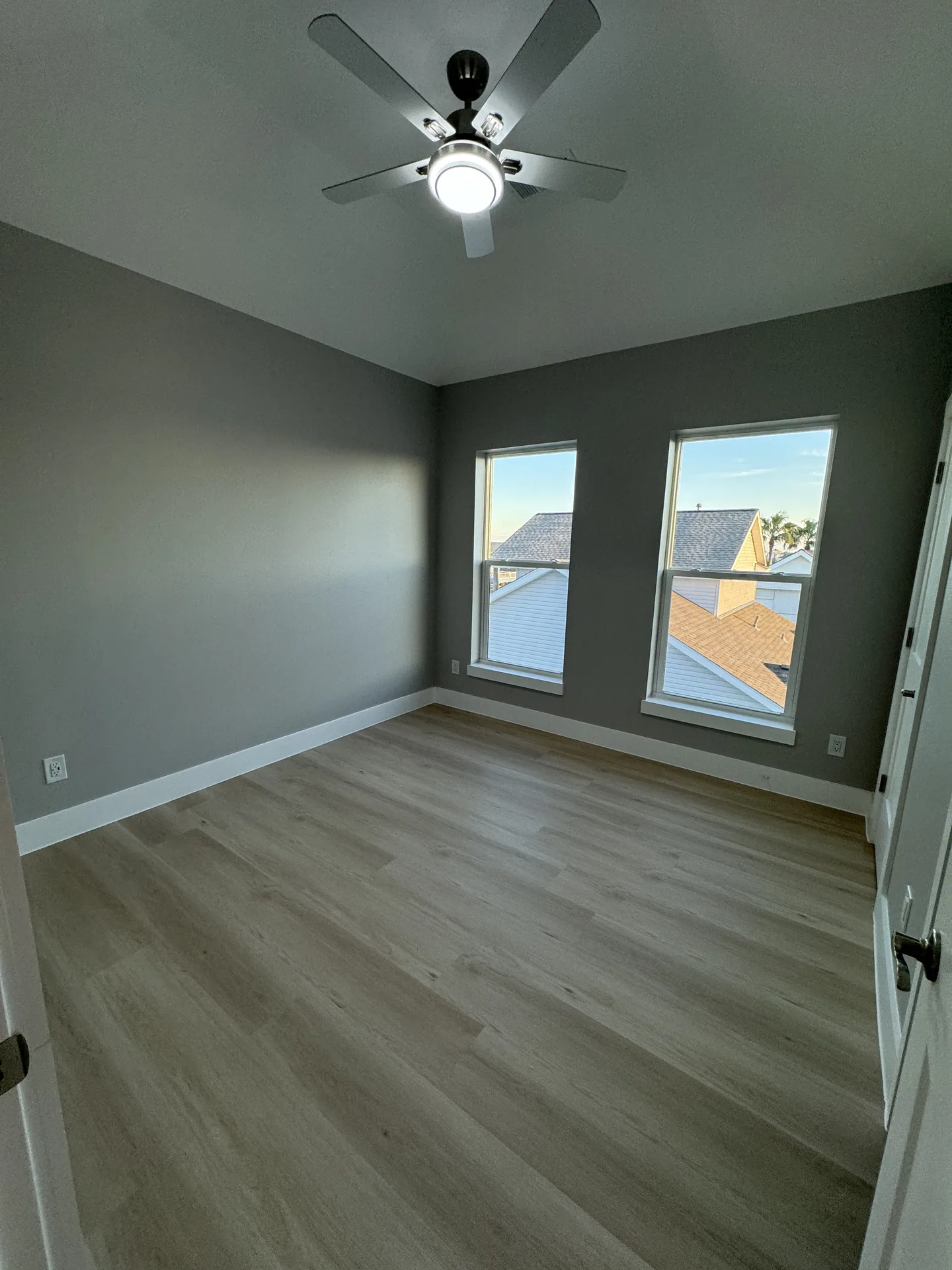 Guest bedroom at Galleon with soft sage walls, wood-look flooring, and windows on two sides