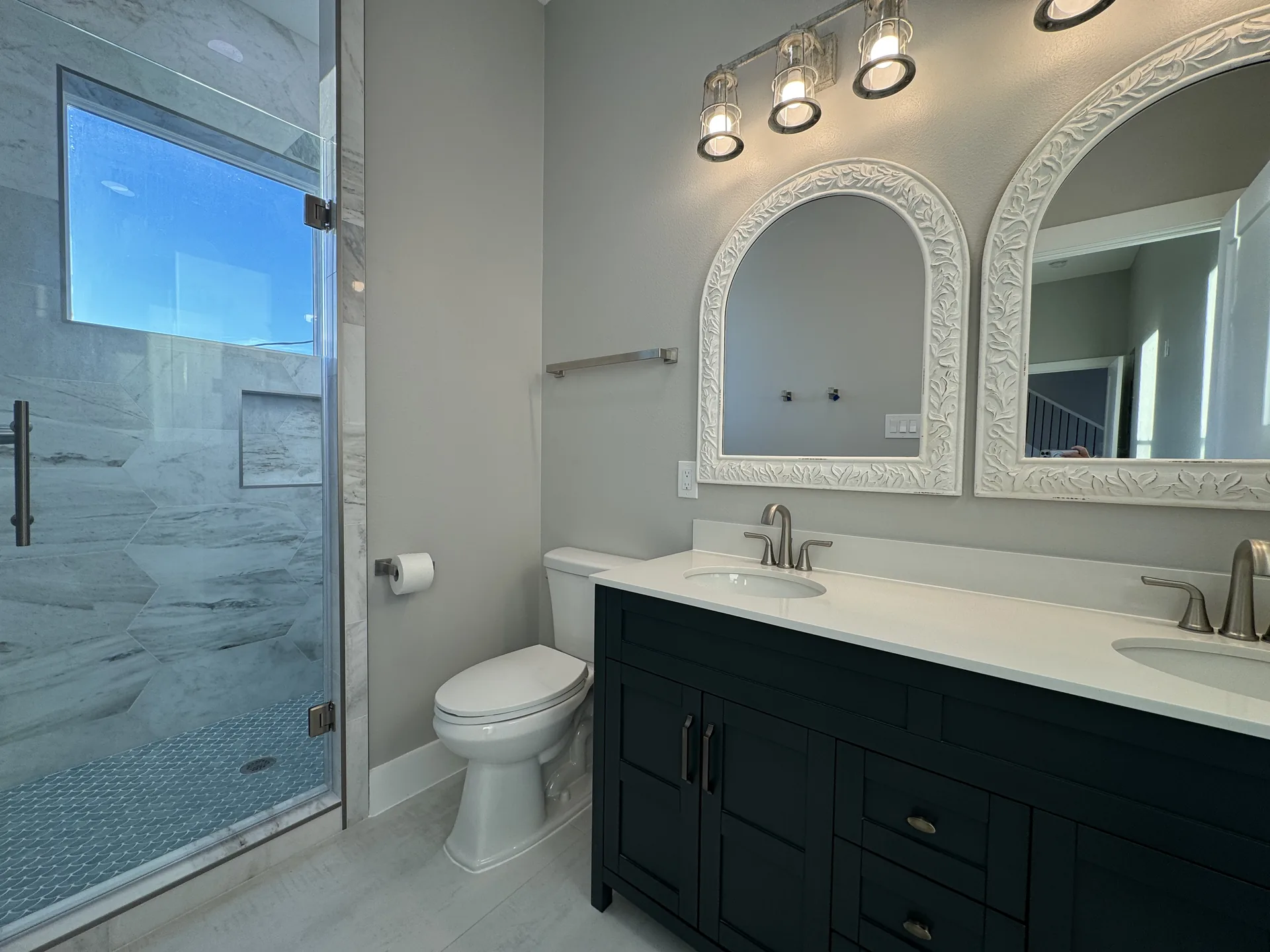 Double vanity bath at Galleon with navy cabinetry, arched mirrors, and a glass-enclosed tile shower