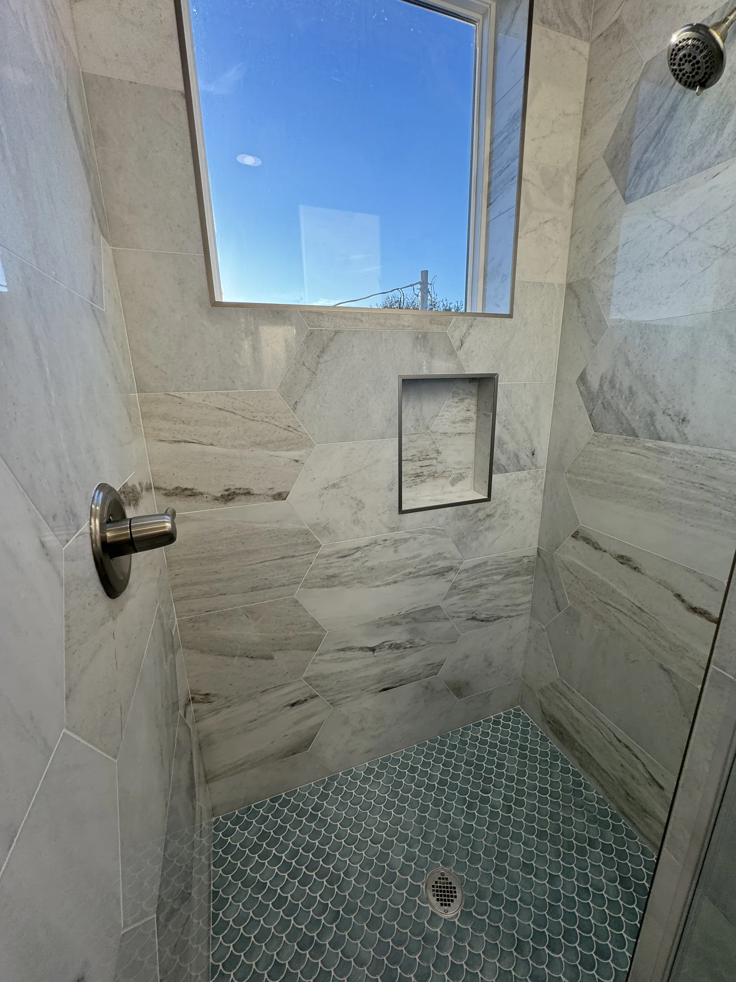 Marble-look tile shower at Galleon with a recessed niche, penny-tile floor, and bronze fixtures