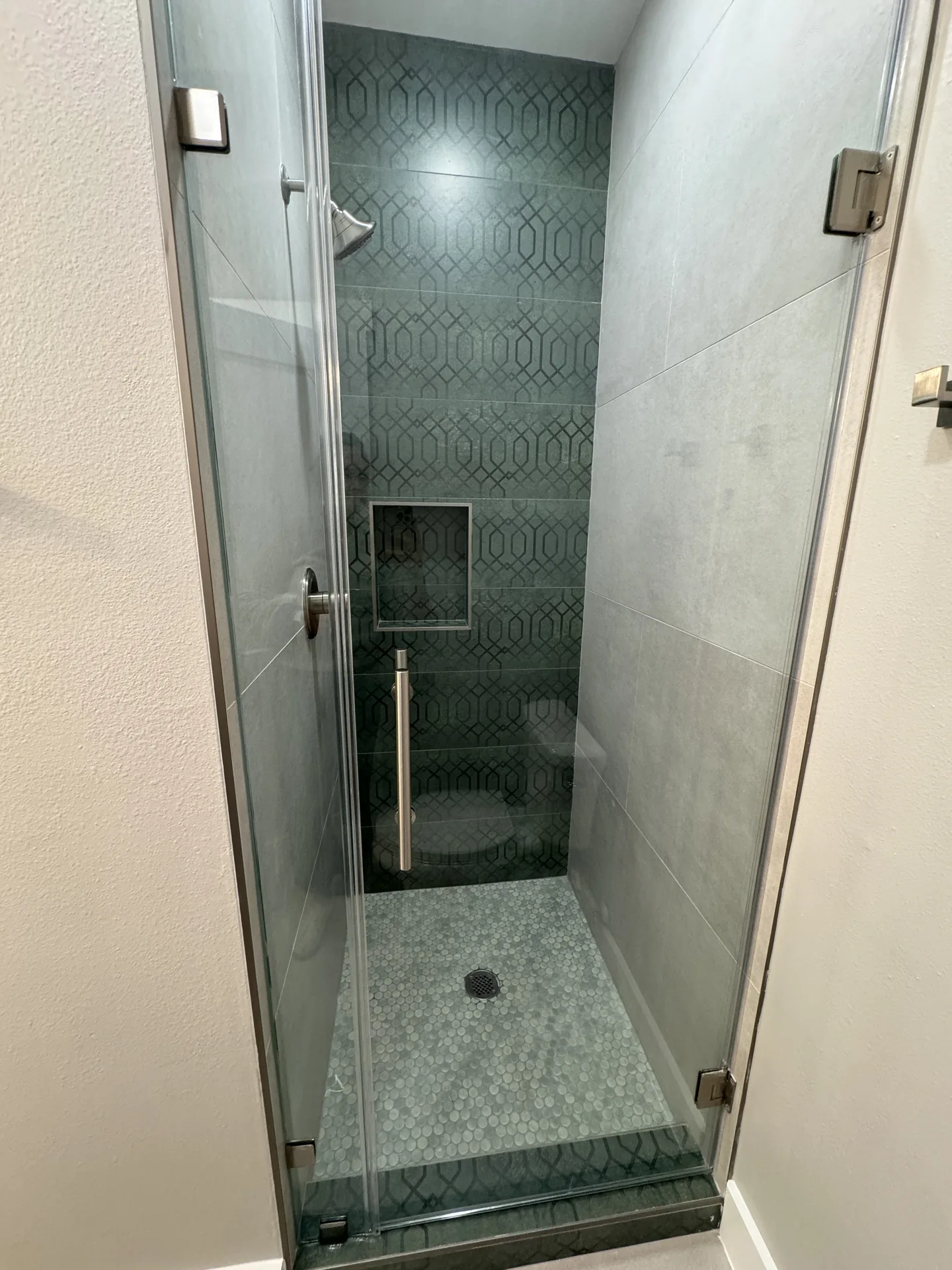 Walk-in shower at Galleon finished in dark patterned tile with a frameless glass enclosure
