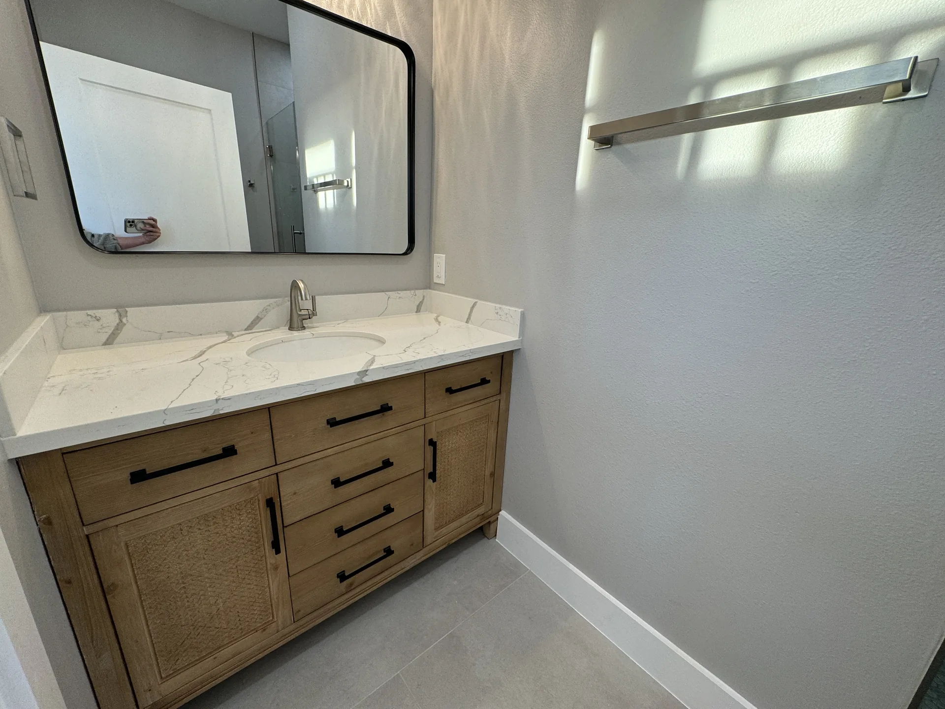 Bathroom vanity at Galleon with a natural wood cabinet, quartz top, and black-framed rectangular mirror