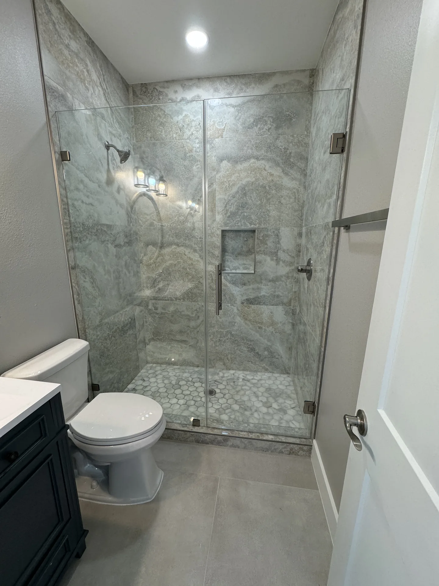 Marble-look walk-in shower at Galleon paired with a navy vanity and bronze shower fittings