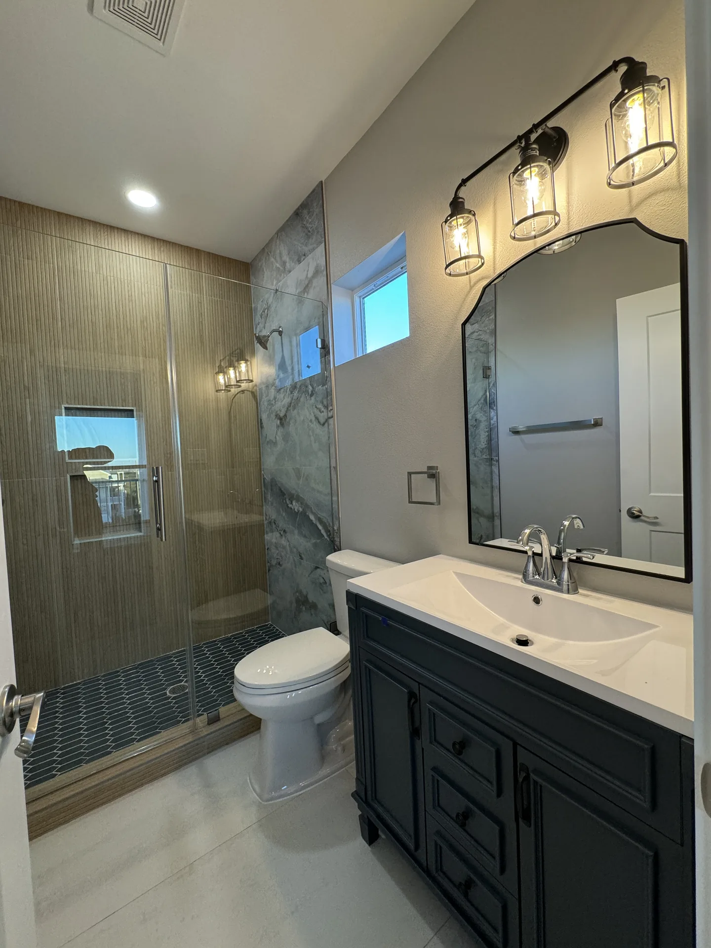 Bathroom at Galleon with a black arched mirror, marble-look shower surround, and dark vanity cabinetry