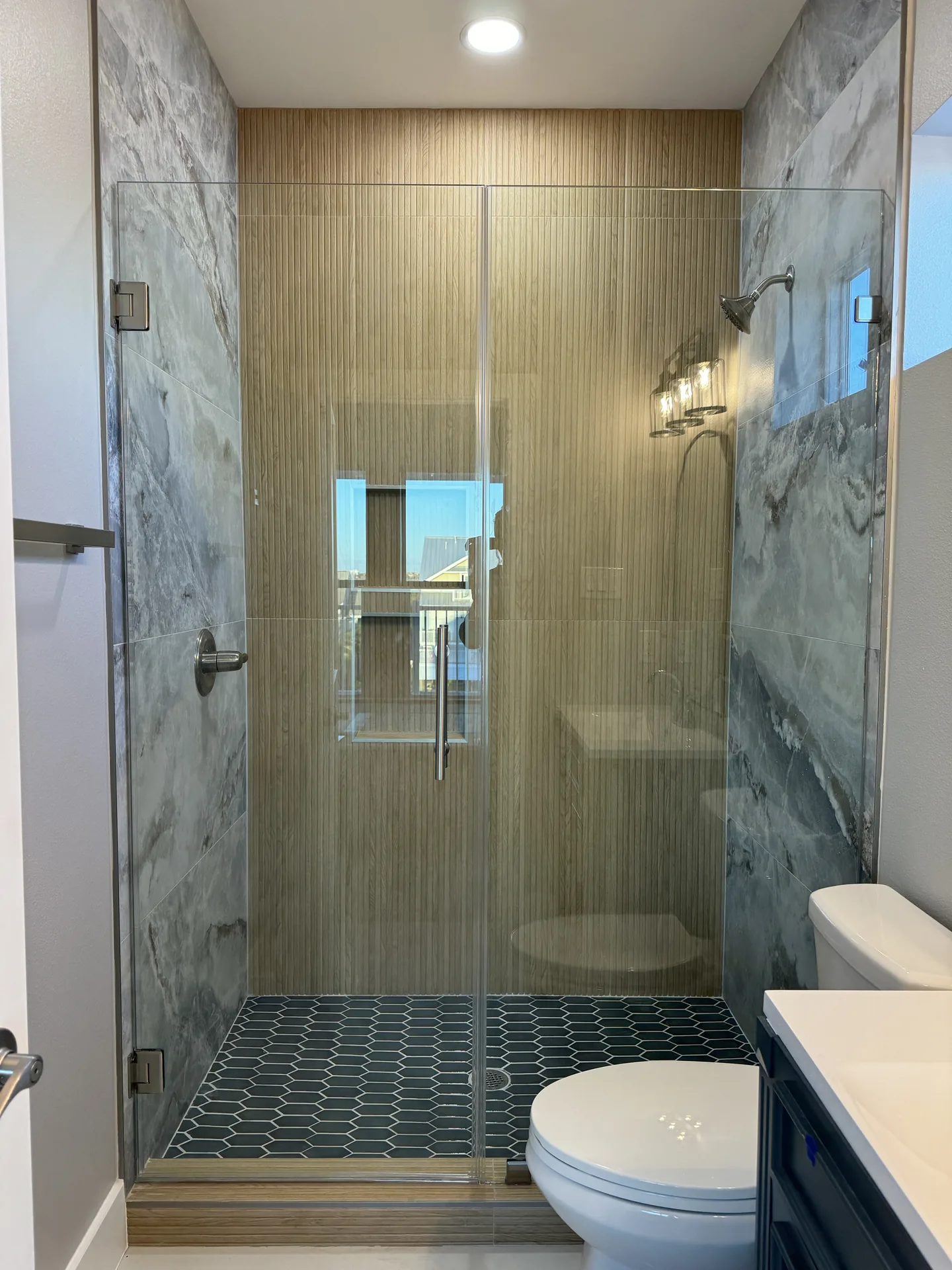 Wood-look tile shower at Galleon with frameless glass, built-in bench, and mosaic floor tile