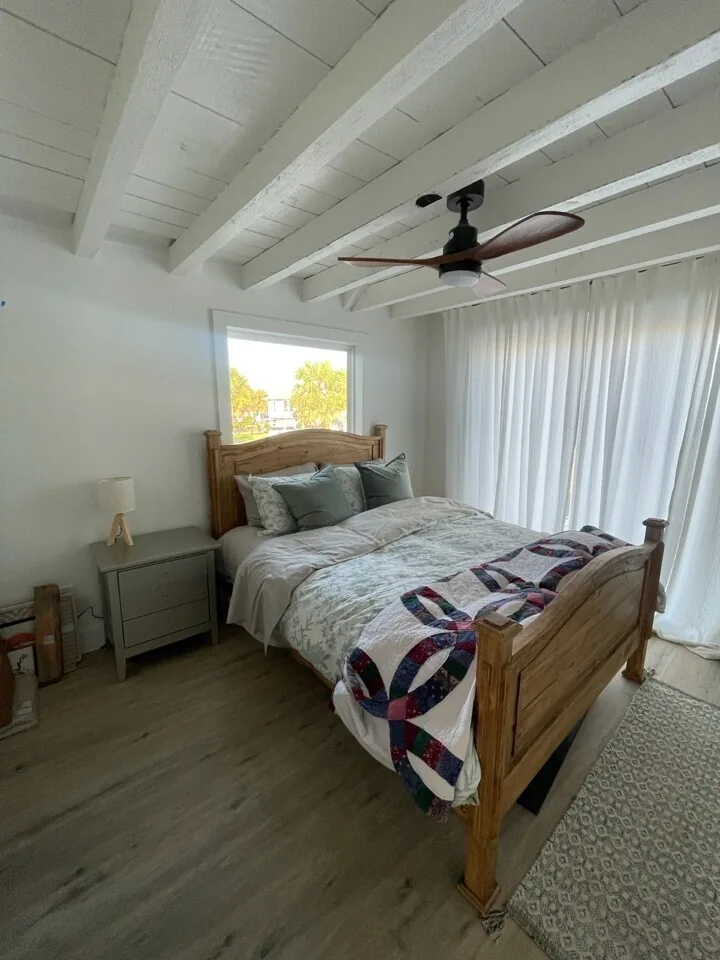 After: renovated guest bedroom with white shiplap ceiling, exposed painted beam, and coastal bedding