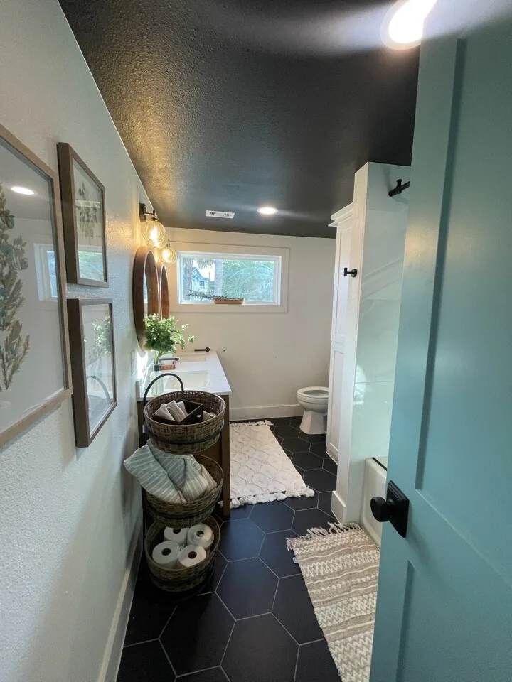 After: renovated hallway with a teal painted ceiling, black hex tile flooring, and a gallery wall