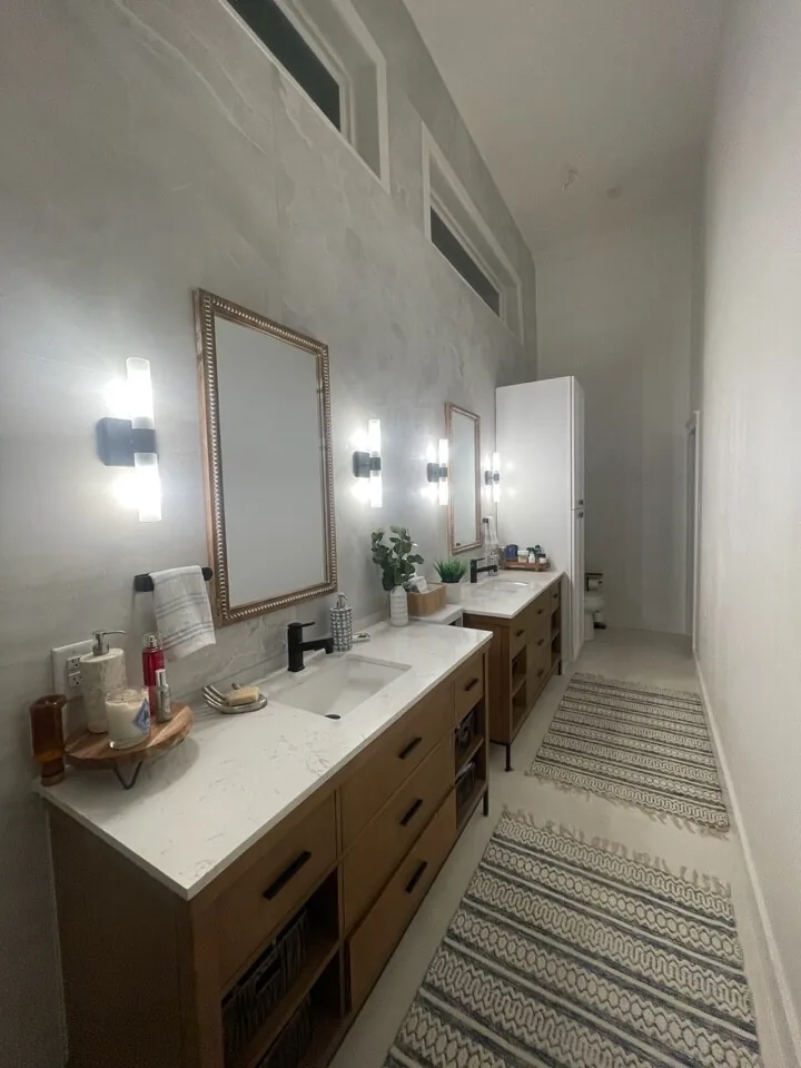 After: renovated double vanity with wood cabinetry, quartz counter, and framed mirrors under sconce lighting