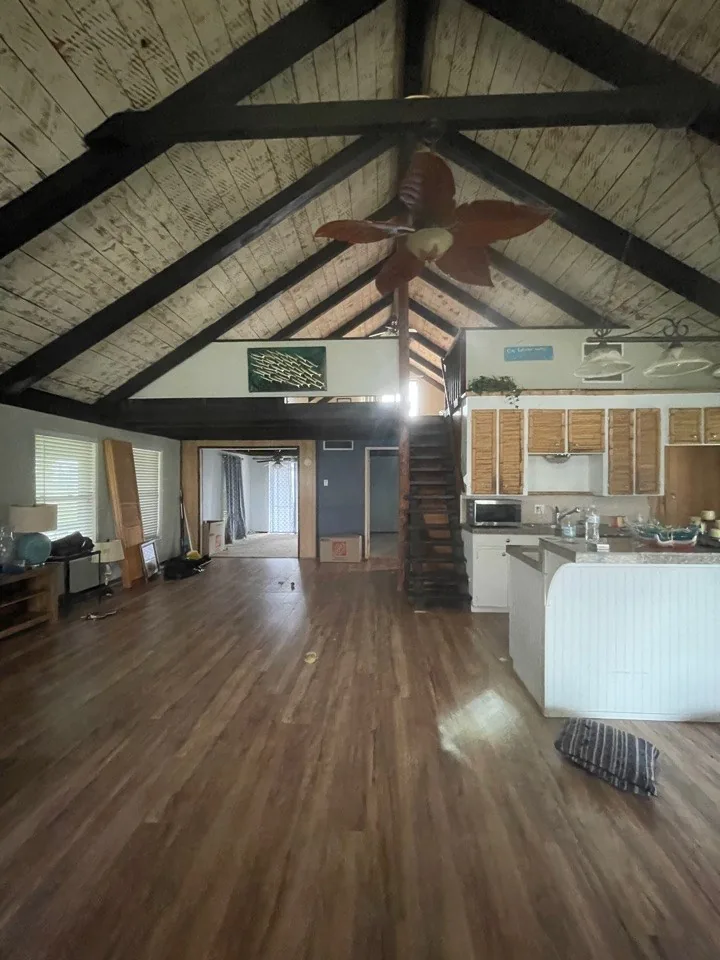Before: original living area with dark stained ceiling boards, heavy beams, and a closed-off plan